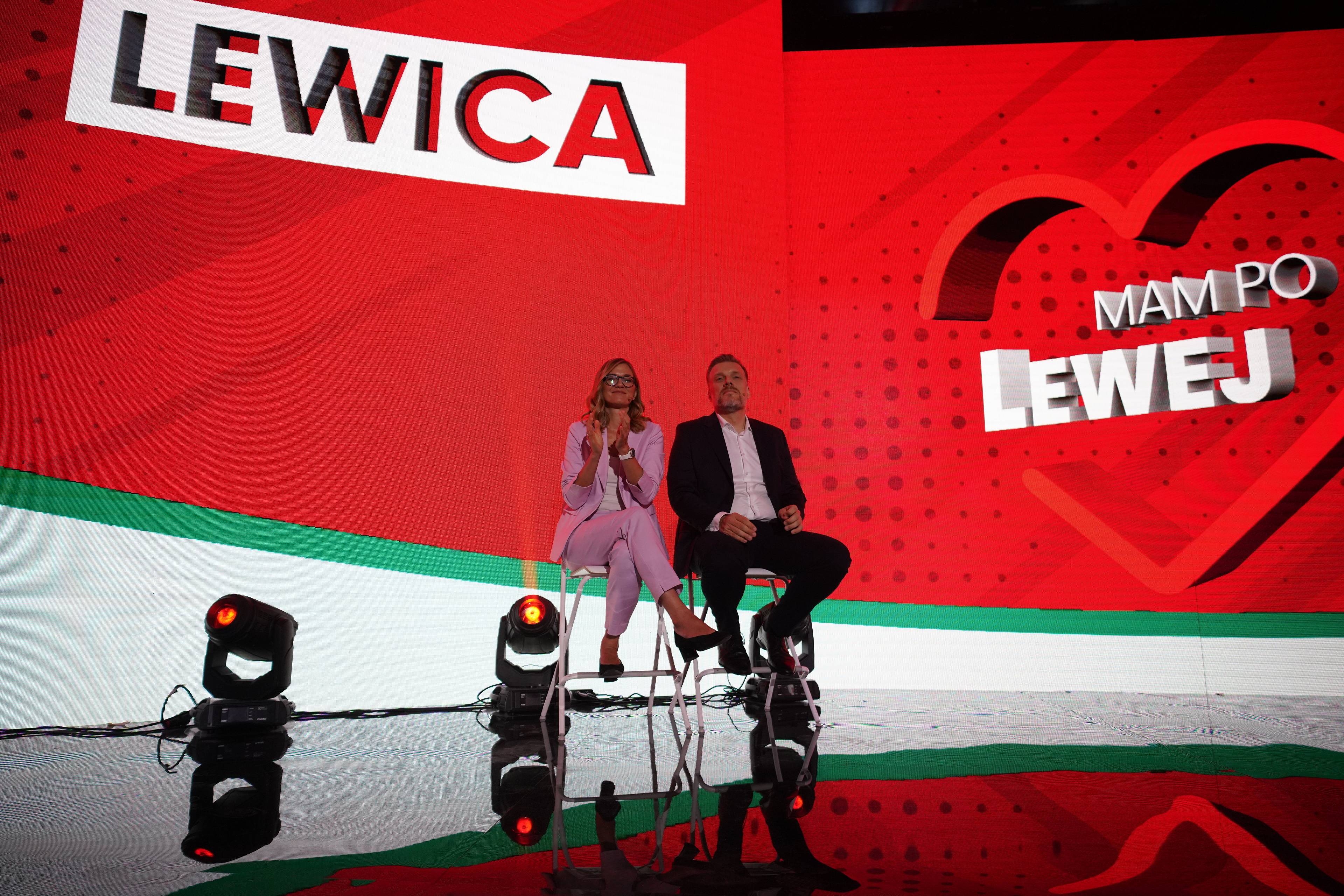 Duża scena z bardzo szerokim świecącym bannerem z napisem "Lewica" i napisem "Mam po lewej" wpisanym w serce. Na scenie dwie osoby, kobieta i mężczyzna