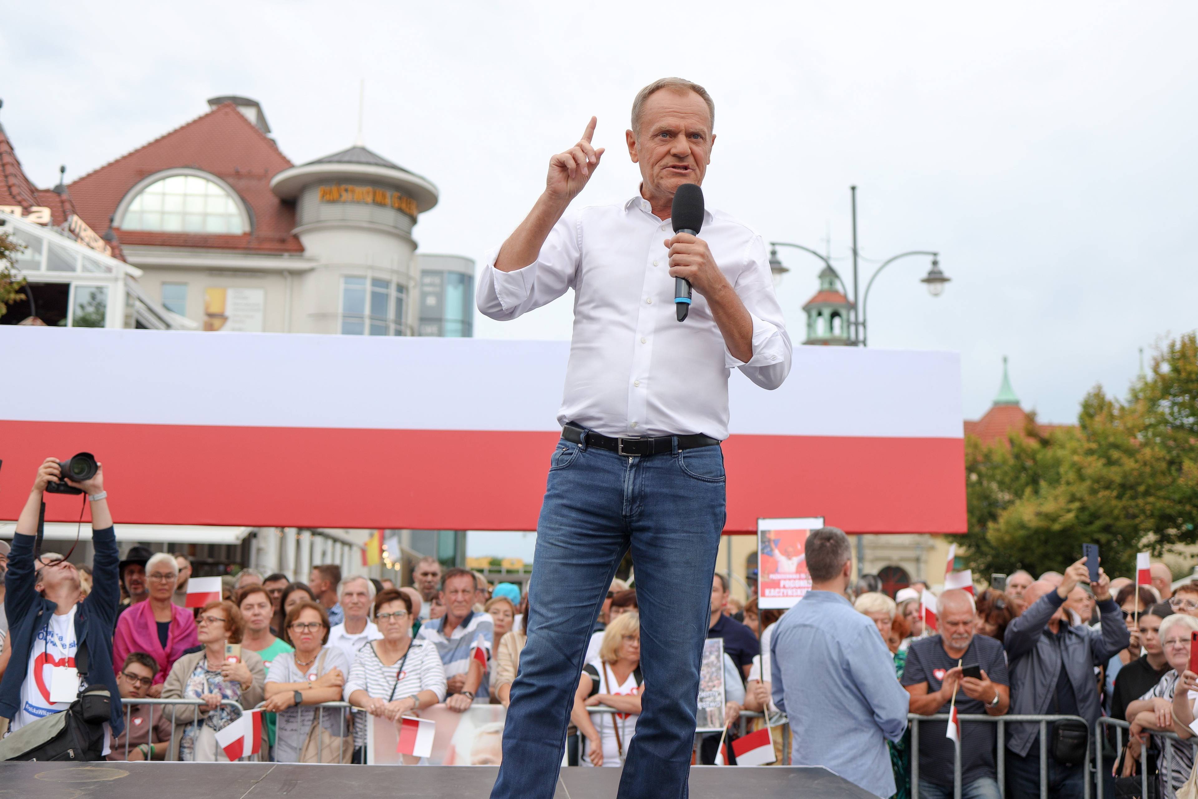 Donald Tusk w białej koszuli z mikrofonem w ręku przemawia do tłumu ludzi