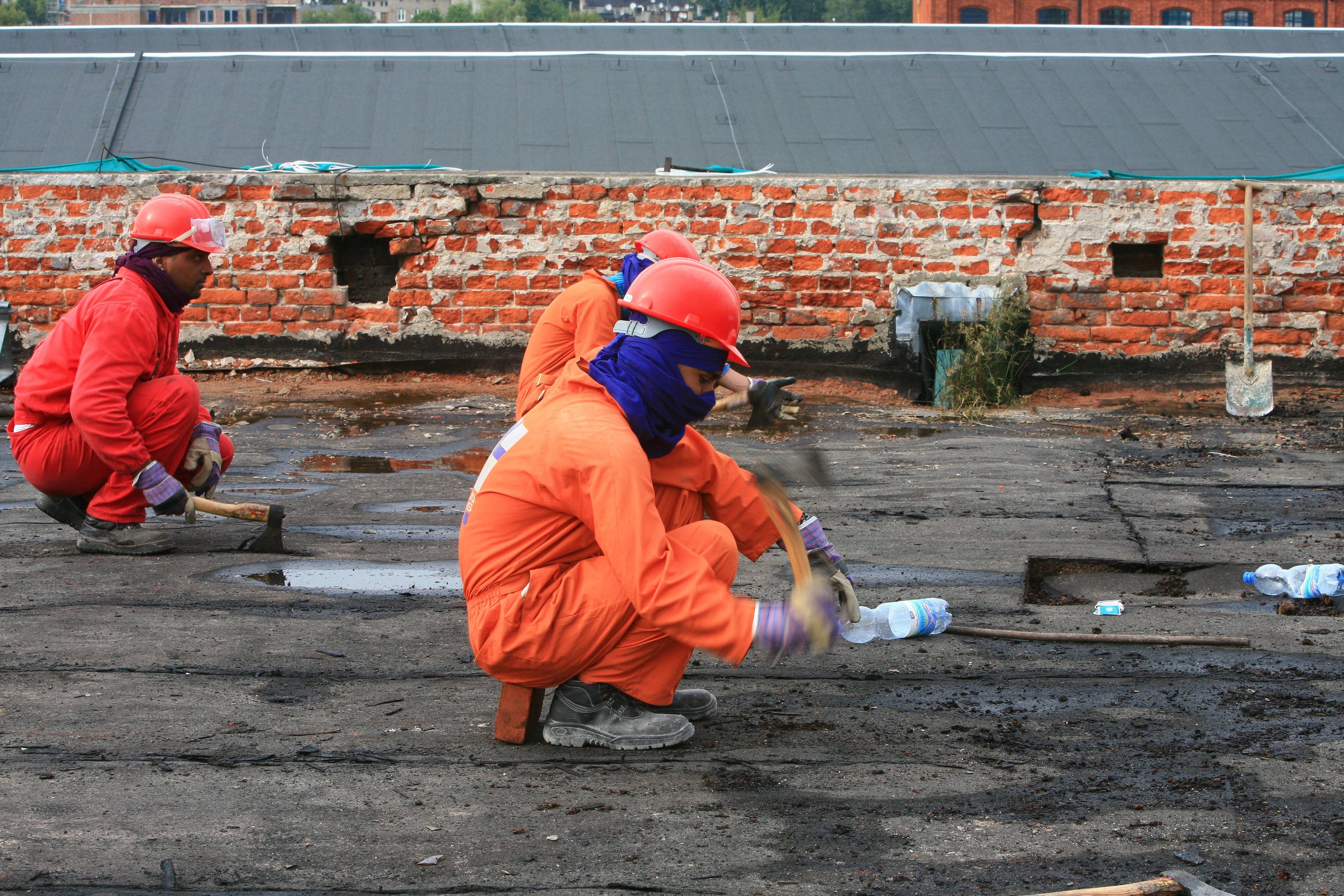 Ciemnoskórzy robotnicy w pomarańczowych strochach pracują na dachu