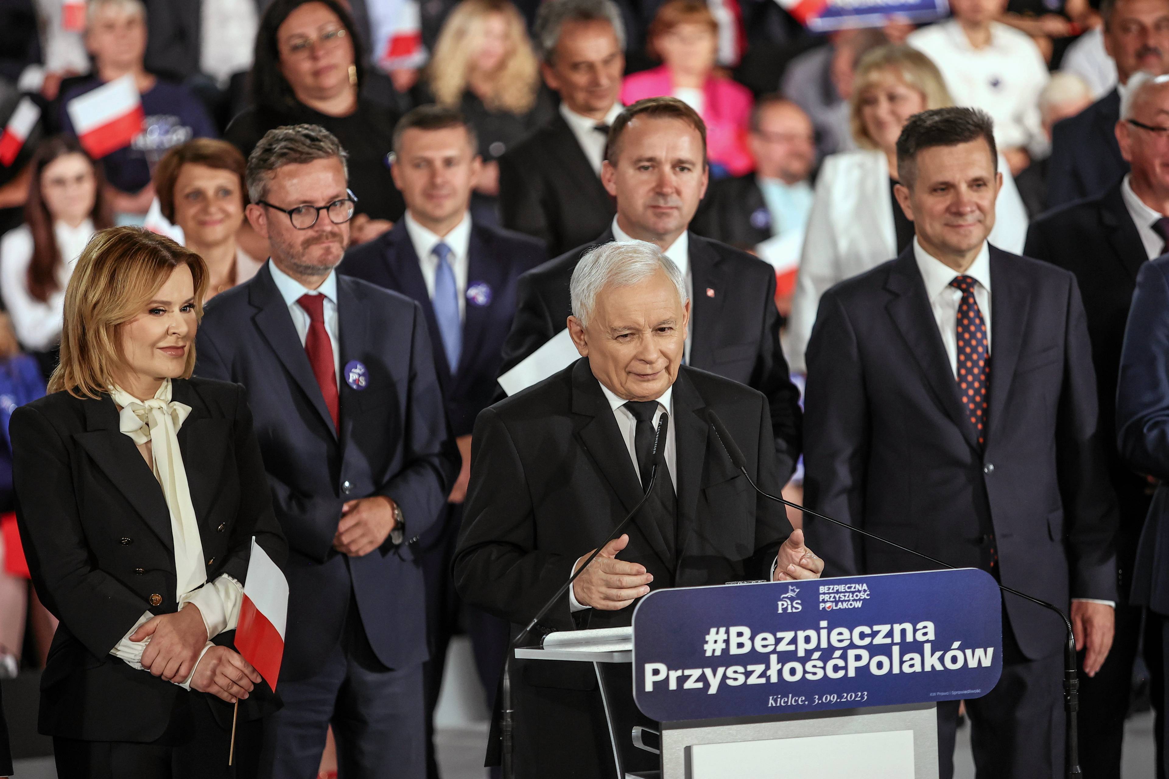 Jarosław Kaczyński za mównicą z napisem #bezpieczna Przyszłość Polaków. Za nim inni politycy