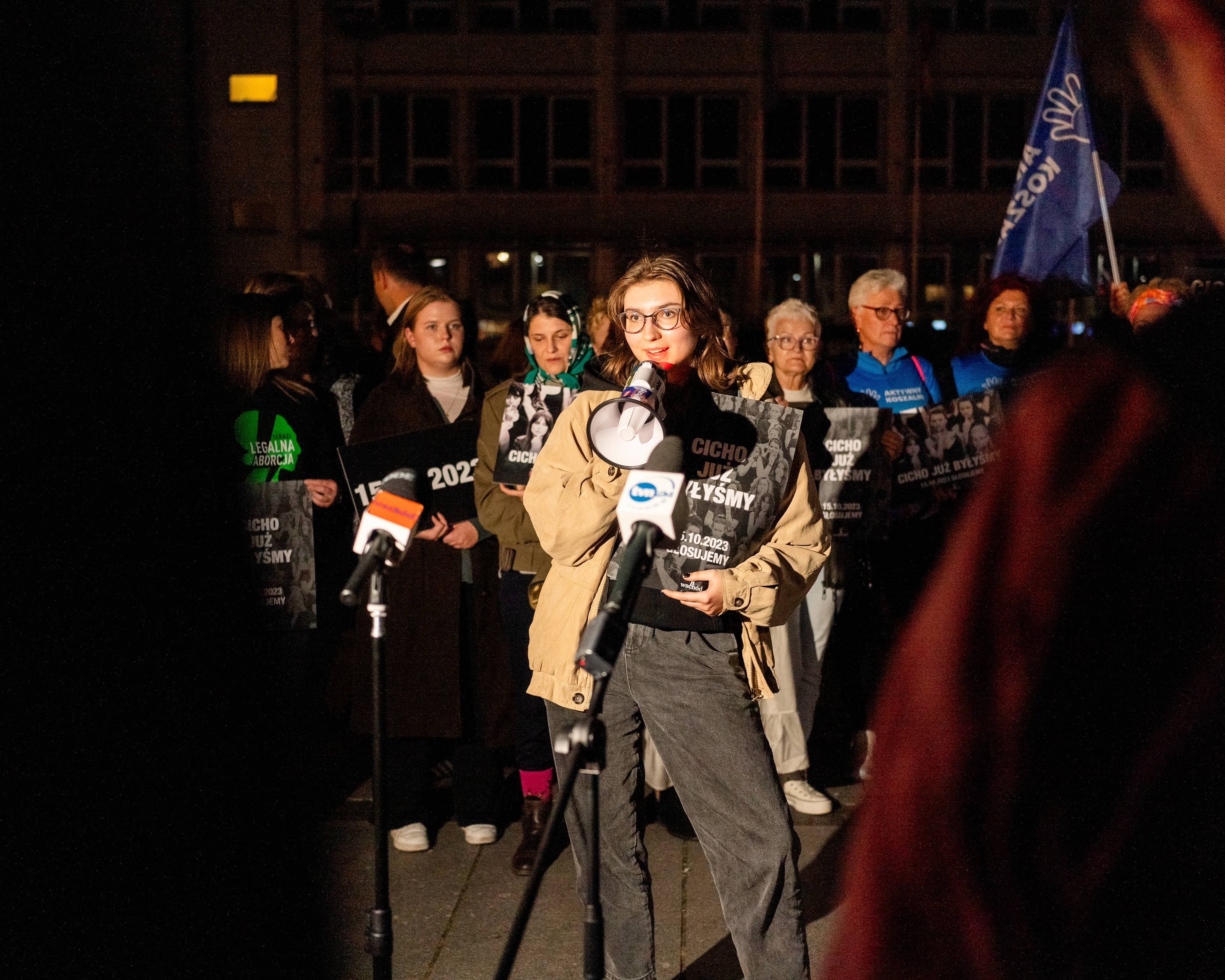 manifestacja uliczna, przemawia dziewczyna z megafonem, trzyma plakat z napisem "Cicho już byłyśmy". Za nią kobiety z podobnymi plakatami