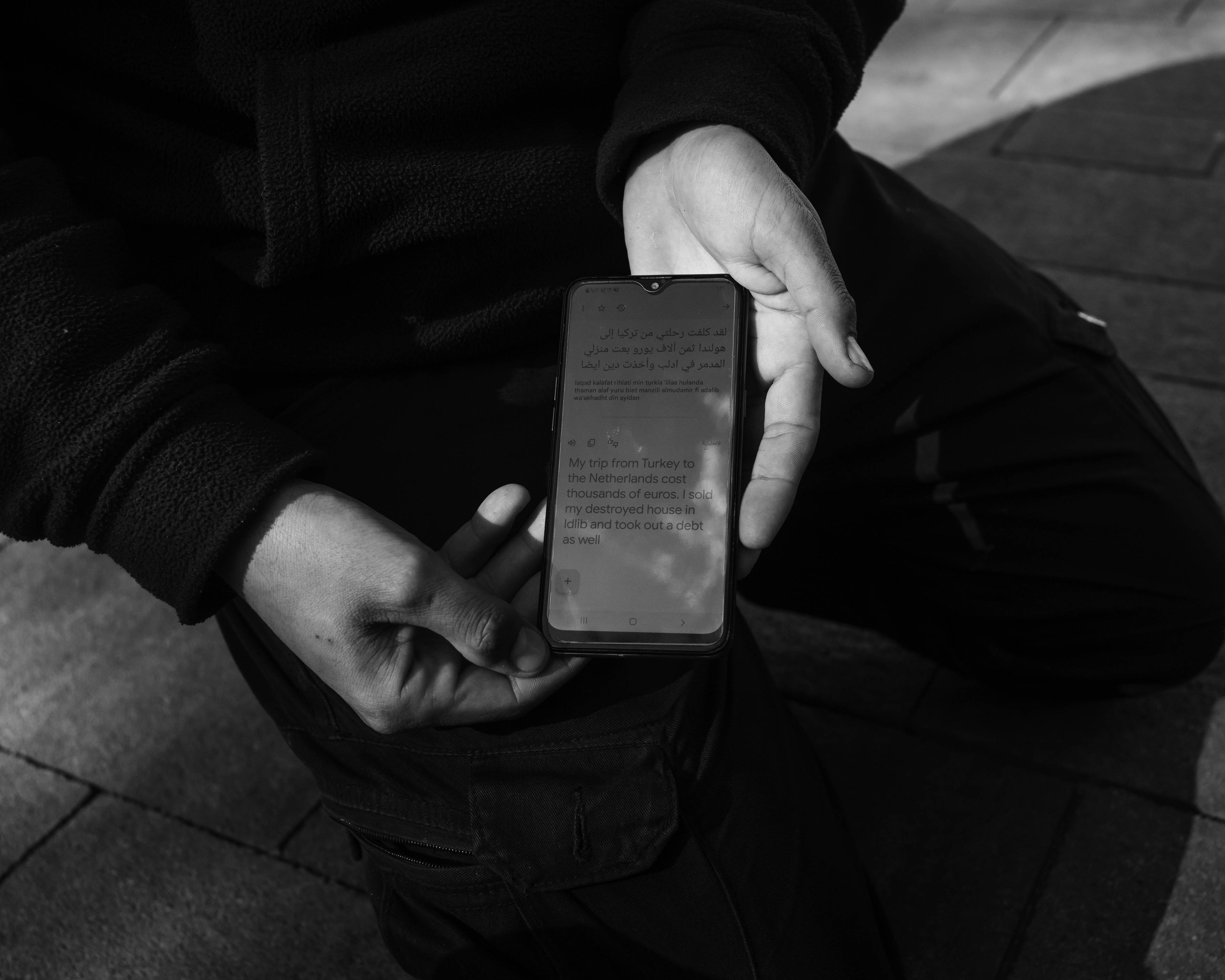 zbliżenie na ręce i ekran smartfona z arabskim tekstem tłumaczonym w translatorze na angielski, zdjęcie czarno-białe