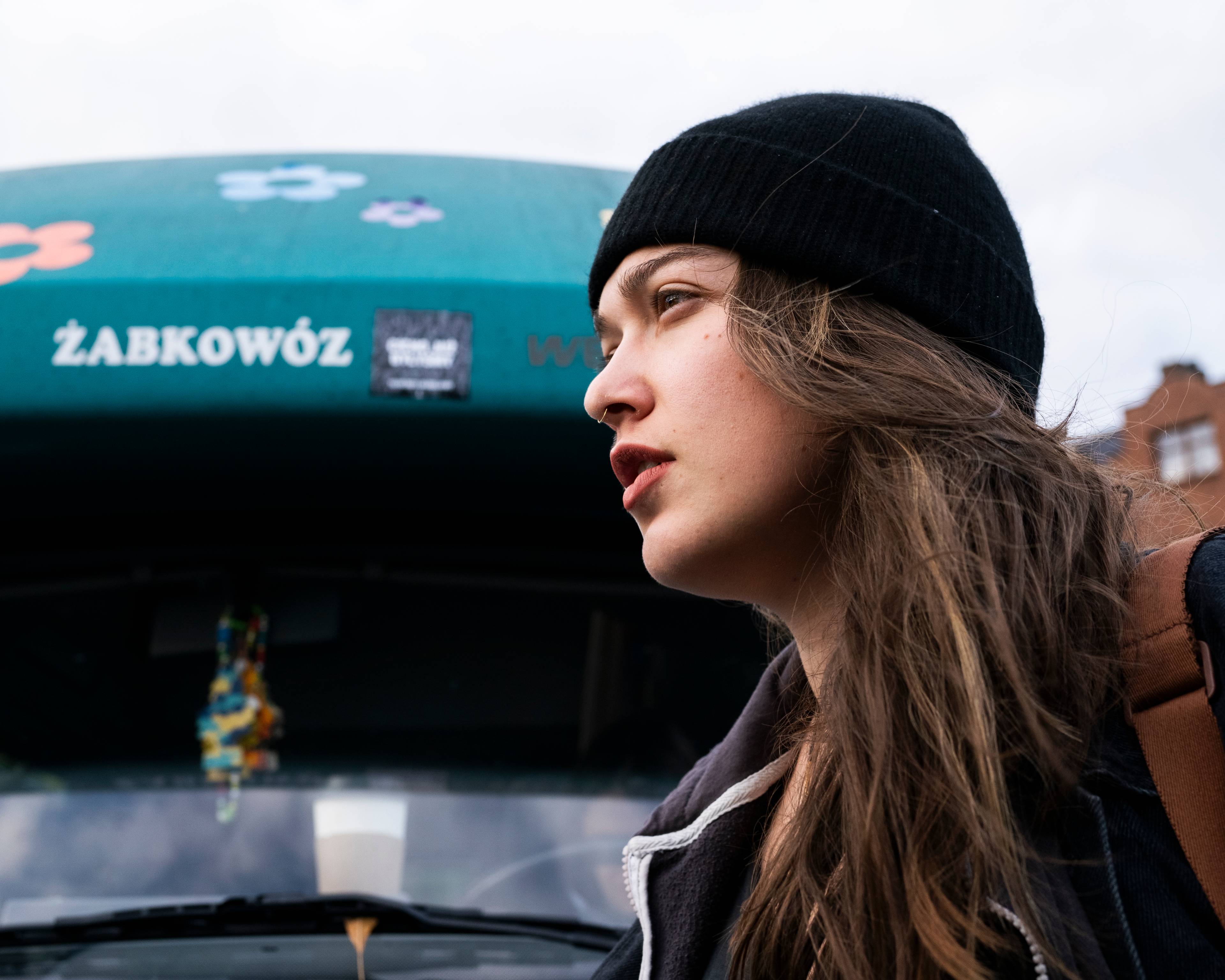 Portret dziewczyny w czarnej czapce, profil, na tle samochodu z napisem Żabkowóz