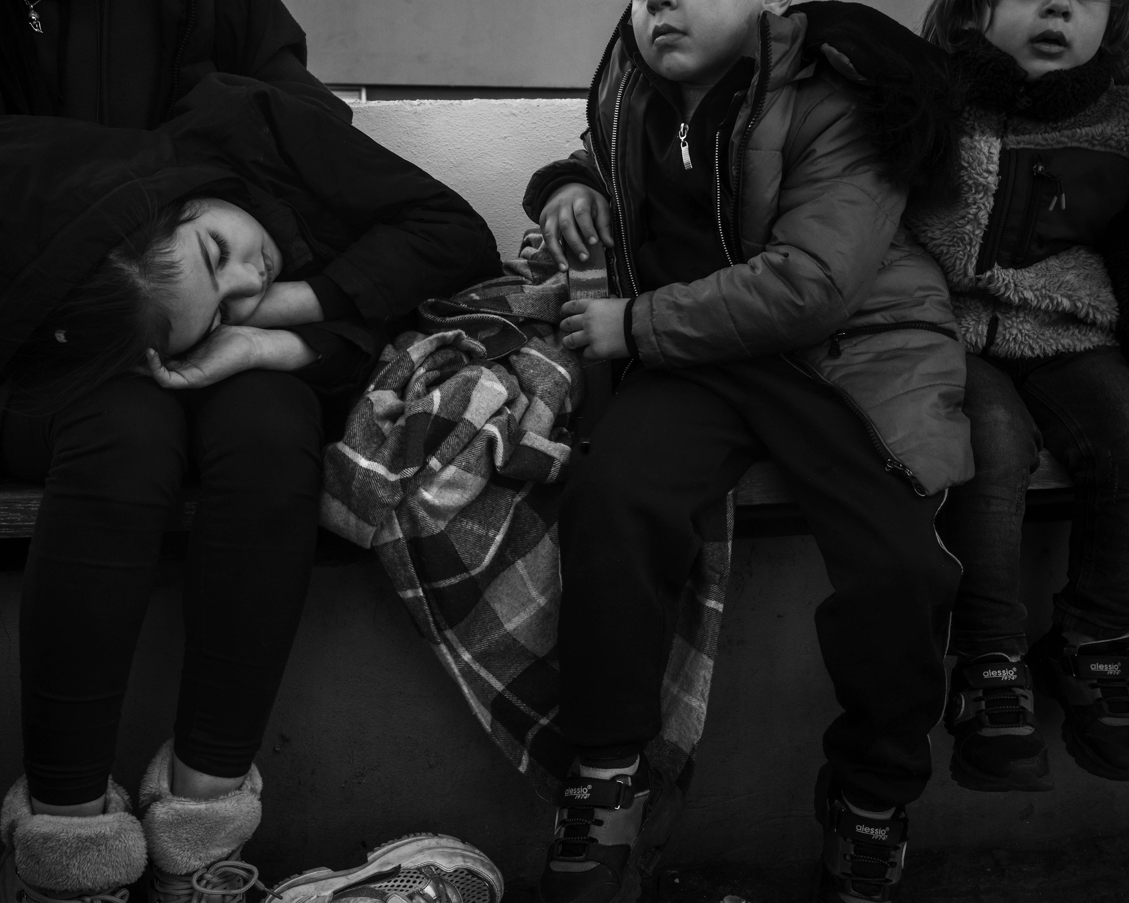 troje dzieci na miejskim murku, jedno śpi z głową na kolanach mamy