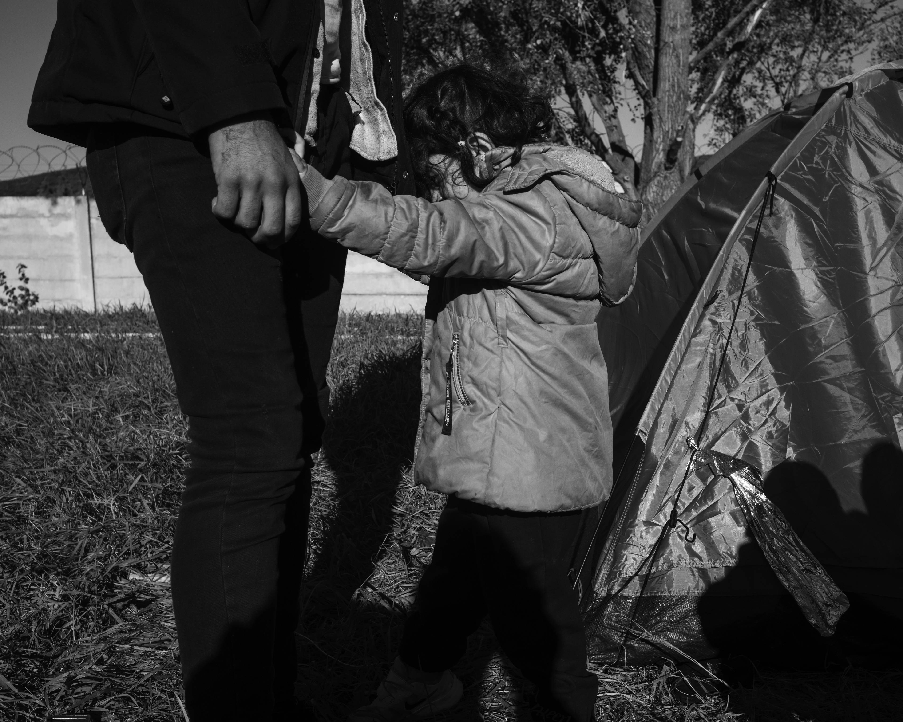 Dziecko stoi przed błyszczącym namiotem trzymając za ręce dorosłego. zdjęcie czarno-białe