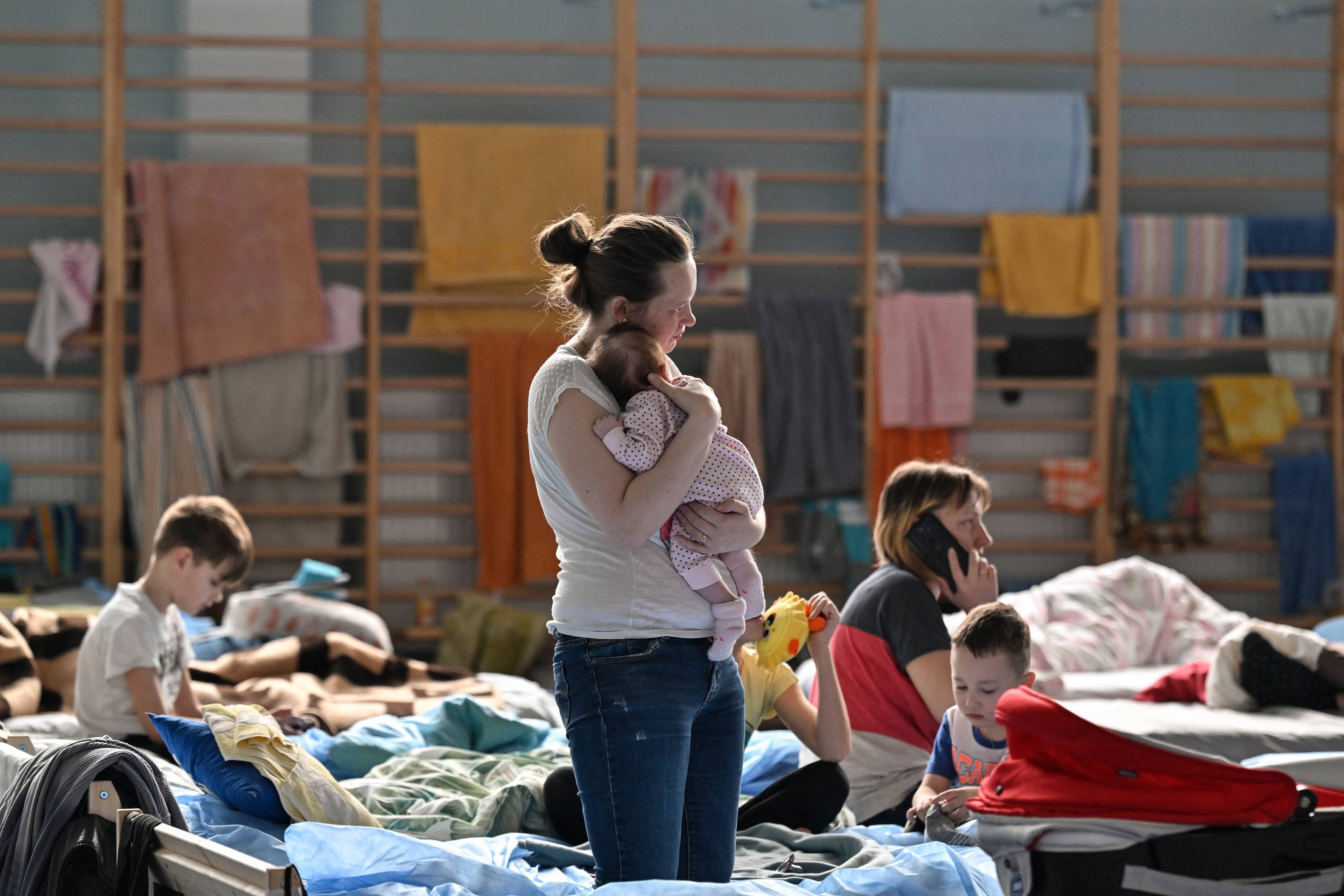 Kobieta trzyma na rekach niemowlaka, w tle łóżka, na których siedzą inne kobiety