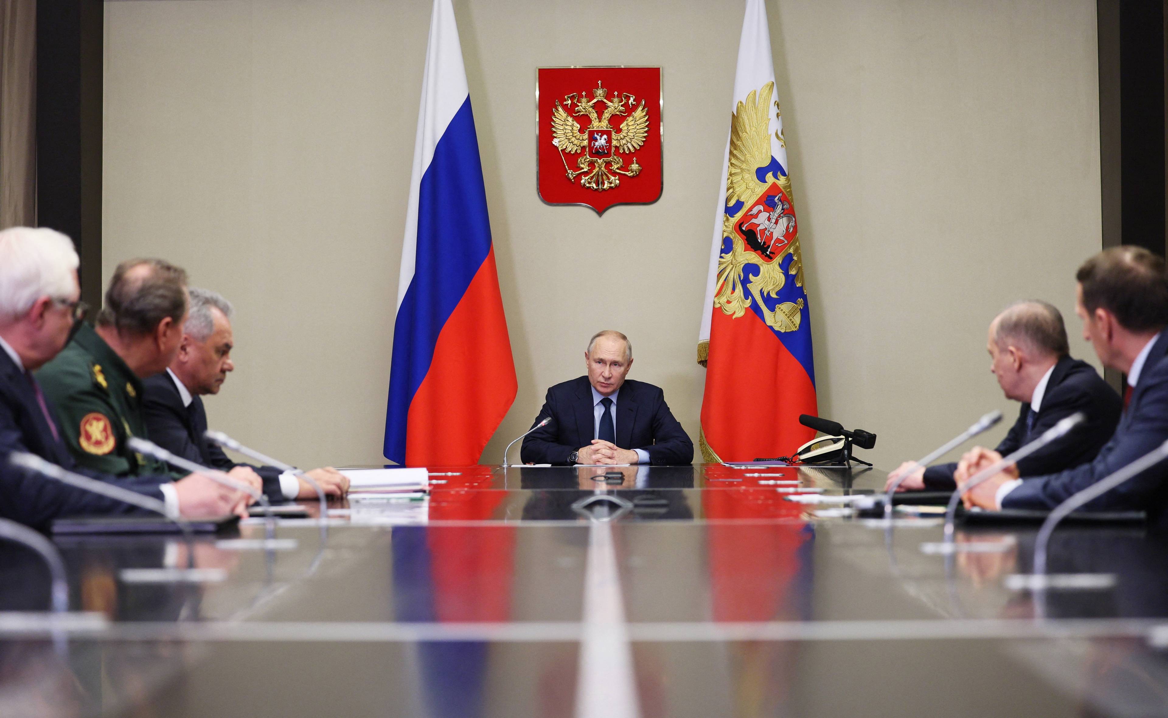 Grupa mężczyzn siedzi przy stole. U szczytu, pod godłem Rosji - Władimir Putin