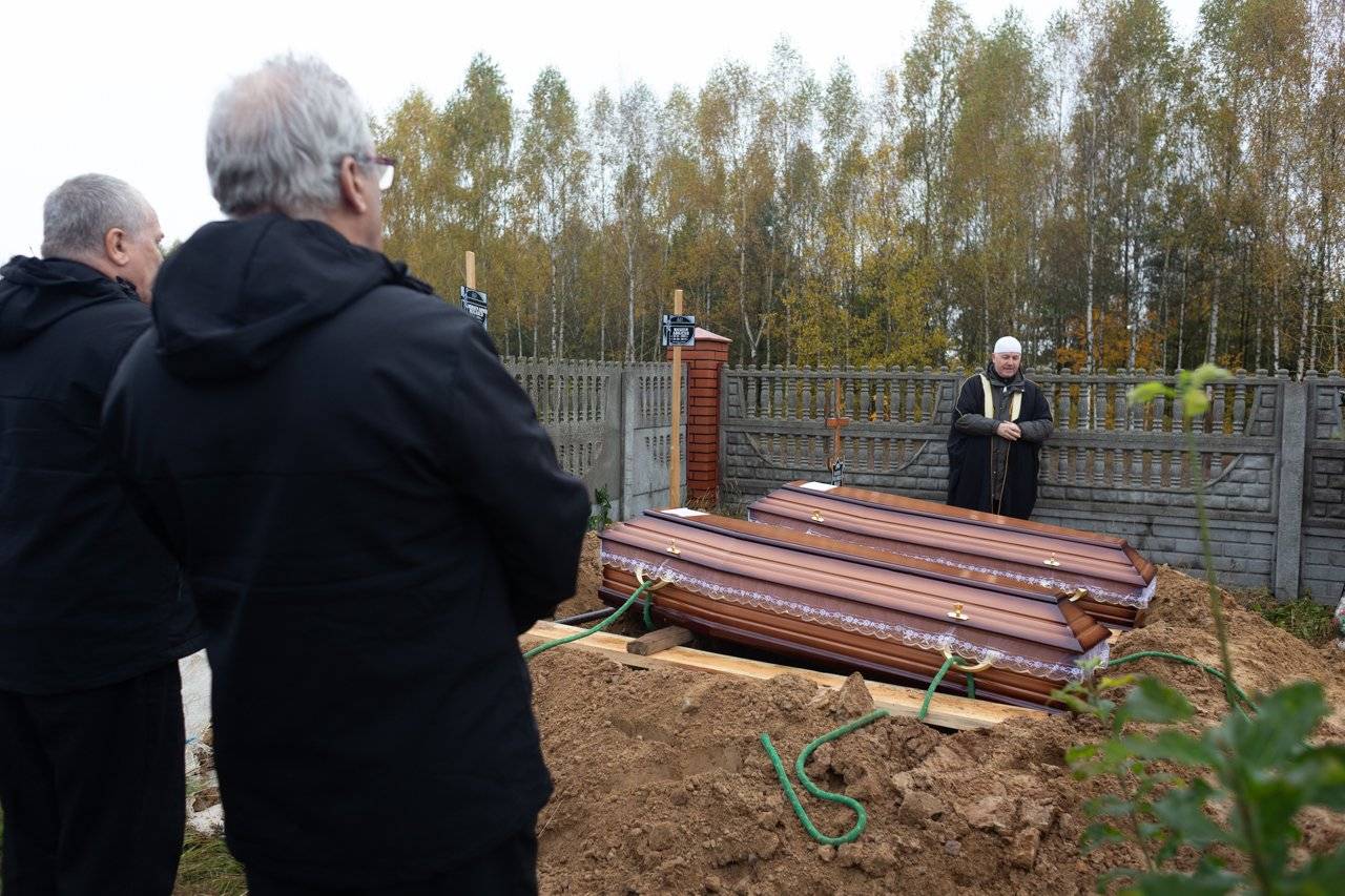 pogrzeb, dwie drewniane trumny gotowe do opuszczenia do mogiły, w głębi modli sie imam
