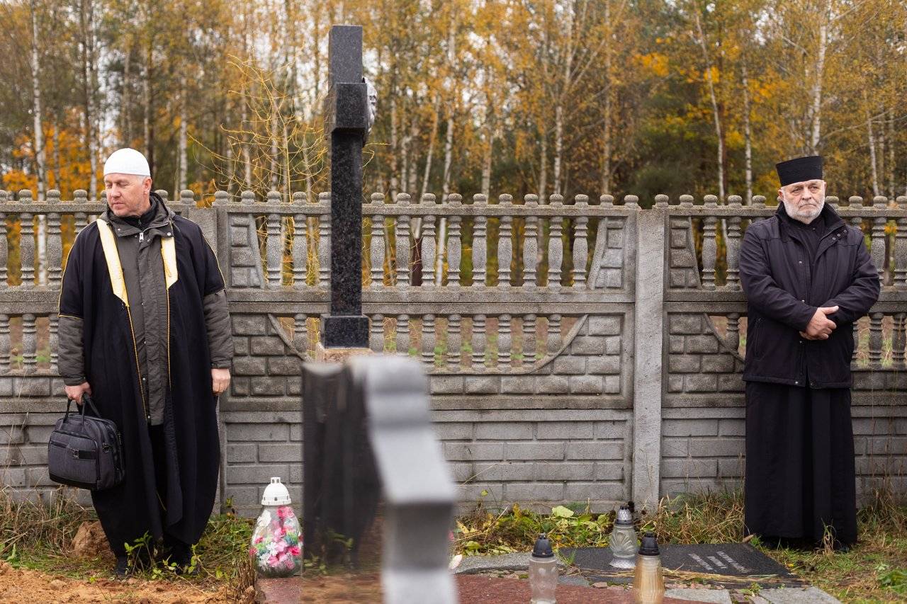 Imam i ksiądz prawosławny stoją na cmentarzu pod płotem