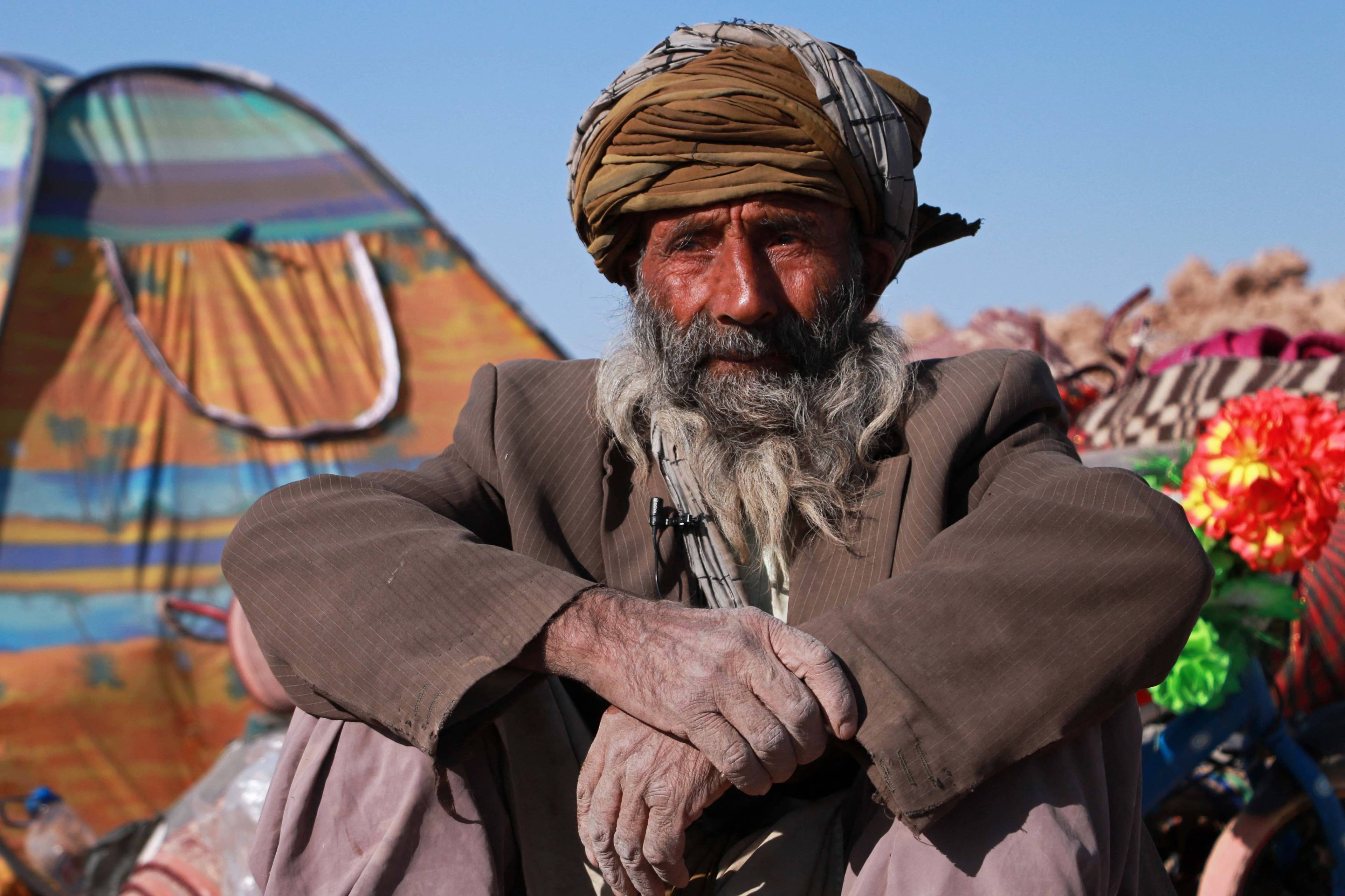 Afgańczyk siedzi na ziemi przed ruinami swego domu