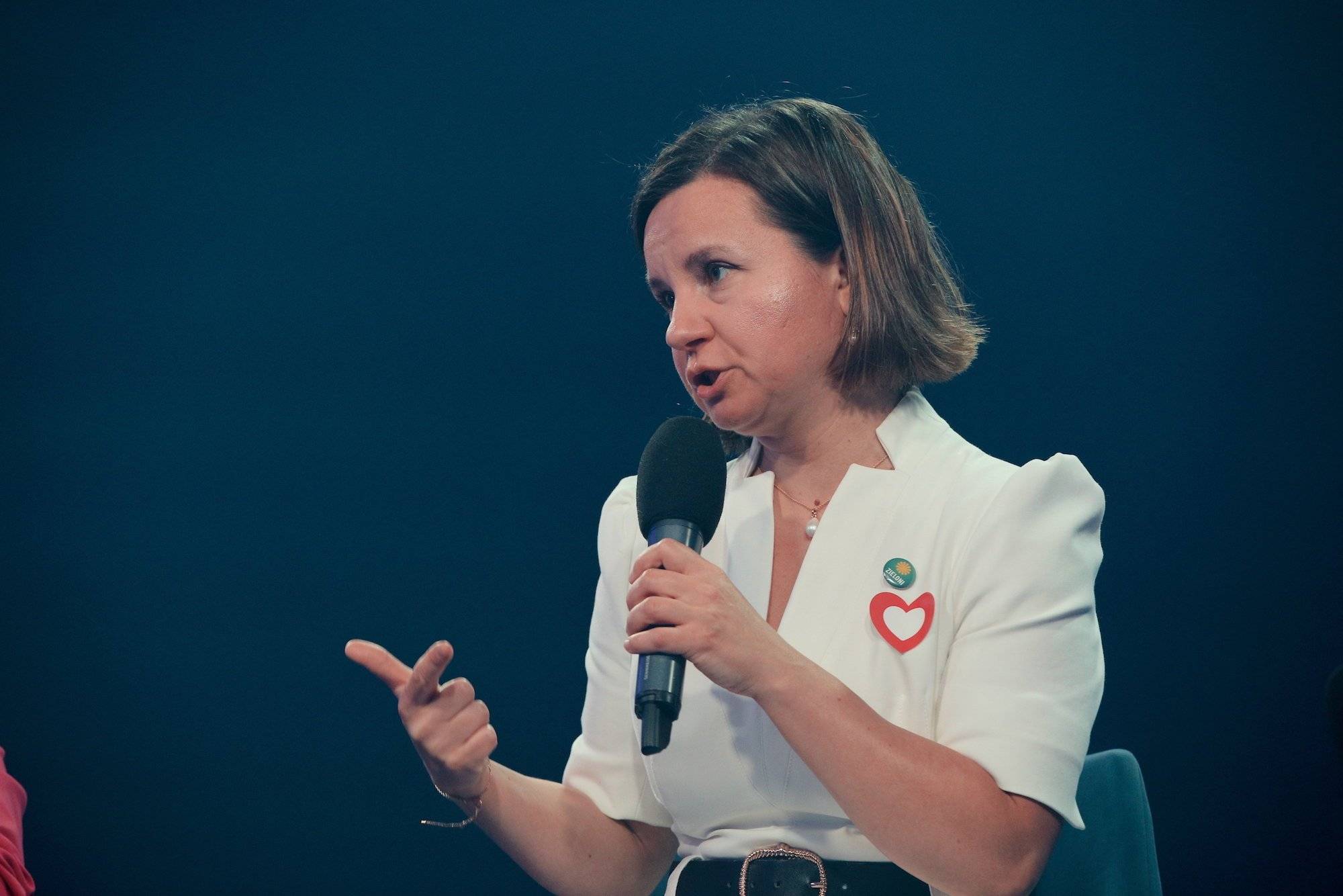 Urszula Zielińska w białej bluzce przemawia do mikrofonu. Siedzi w zielonym fotelu.