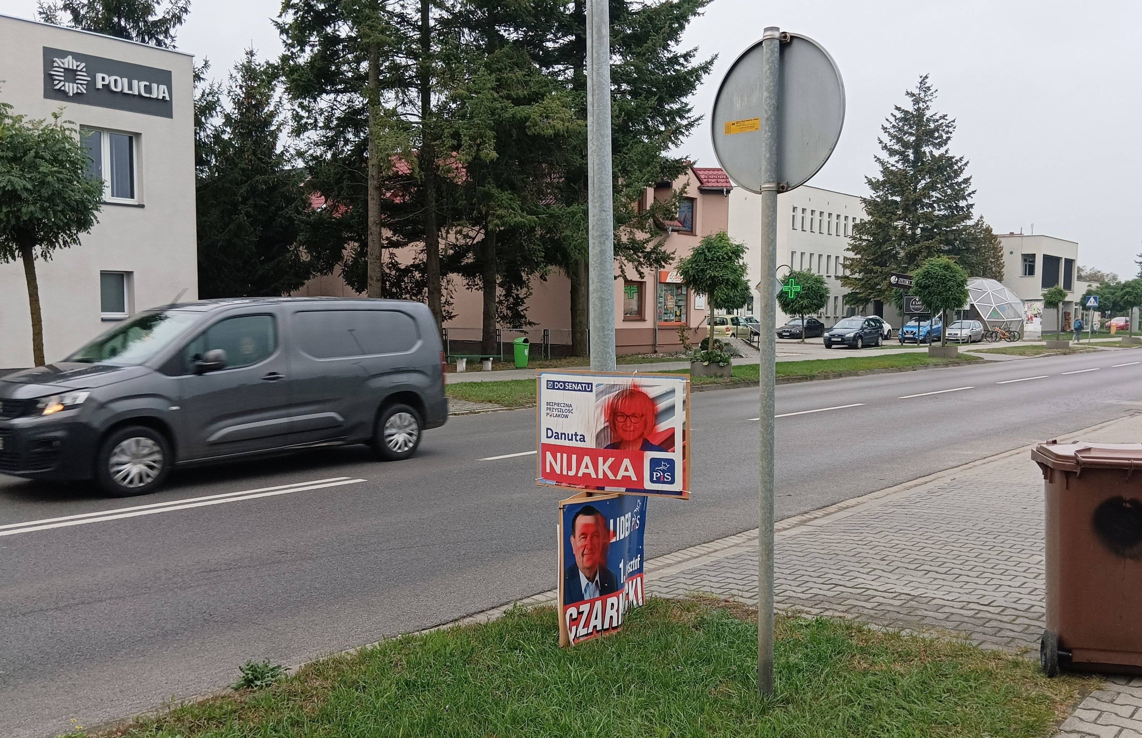 ulica Zbąszynia, widać dwa plakaty powieszone na słupie z kandydatami PiS z zamalowanymi czerwoną farbą twarzami, na dolnym plakacie widoczne nazwisko: Danuta Nijaka. Po drugiej stronie drogi posterunek policji.
