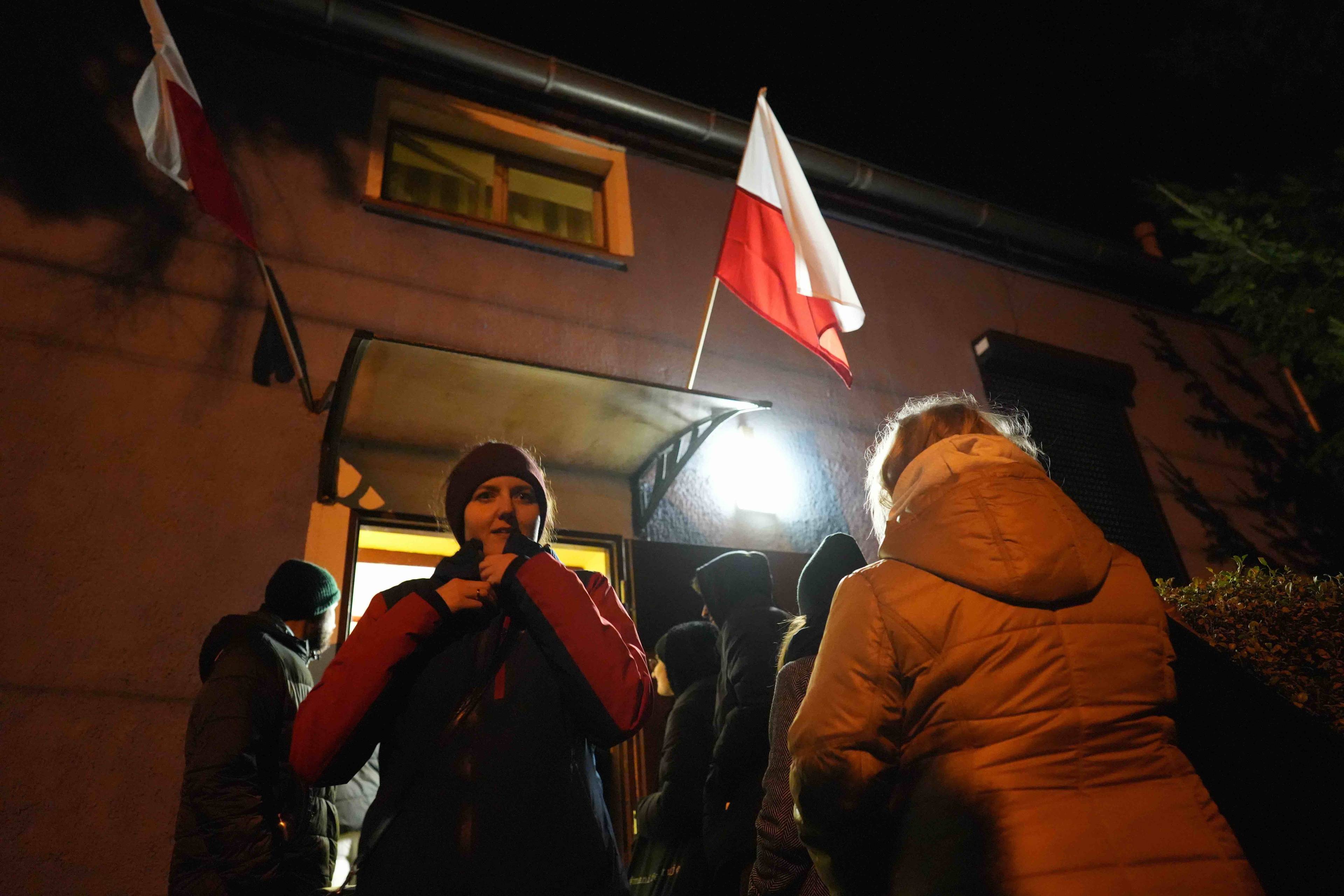 Tłum oczekuje nocą przed wejściem do lokalu wyborczego, nad którym powiewa biało-czerwona flaga.