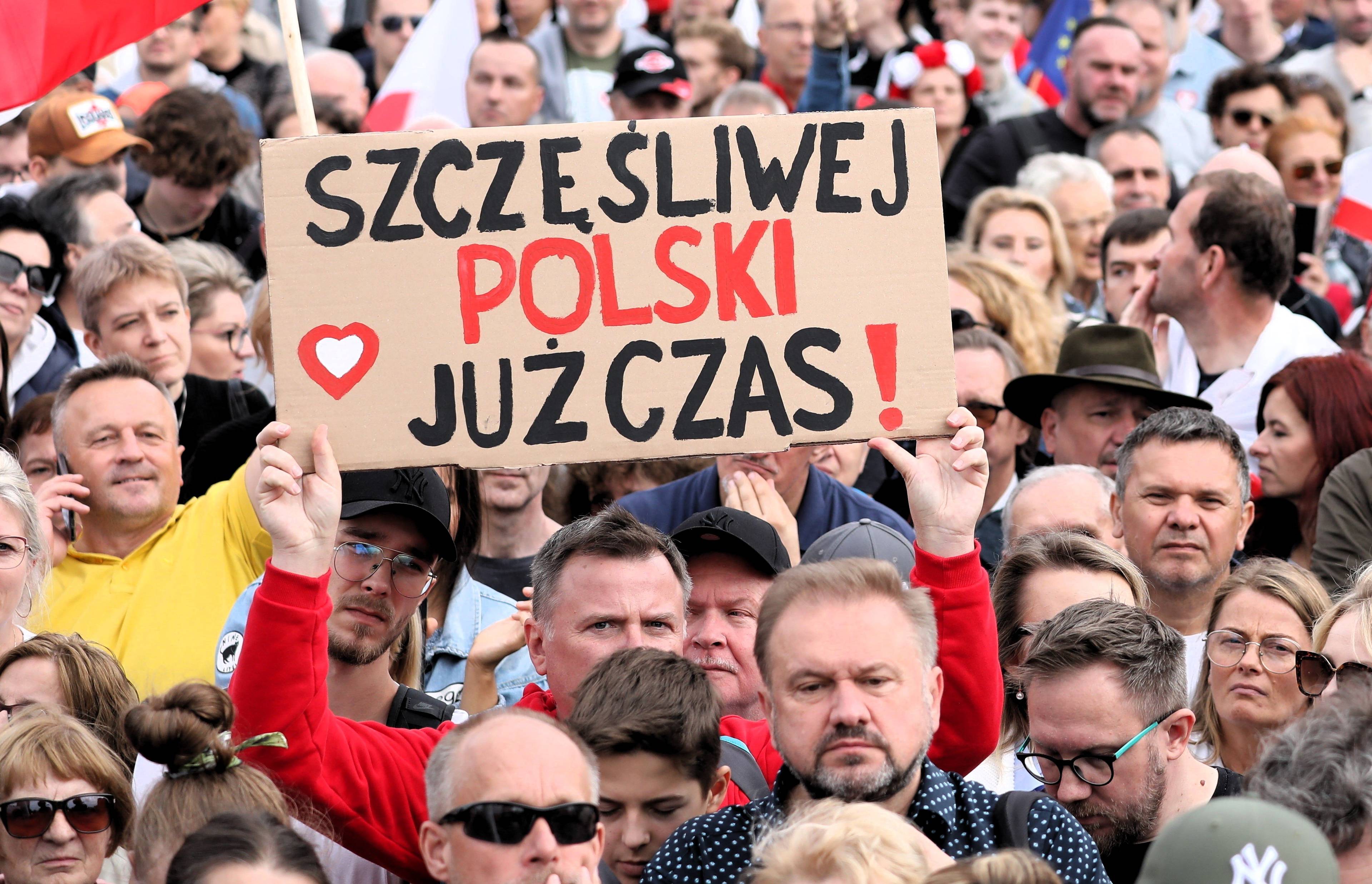 Tłum ludzi, mężczyzna trzyma plansze z napisem Szczęśliwej Polski już czas