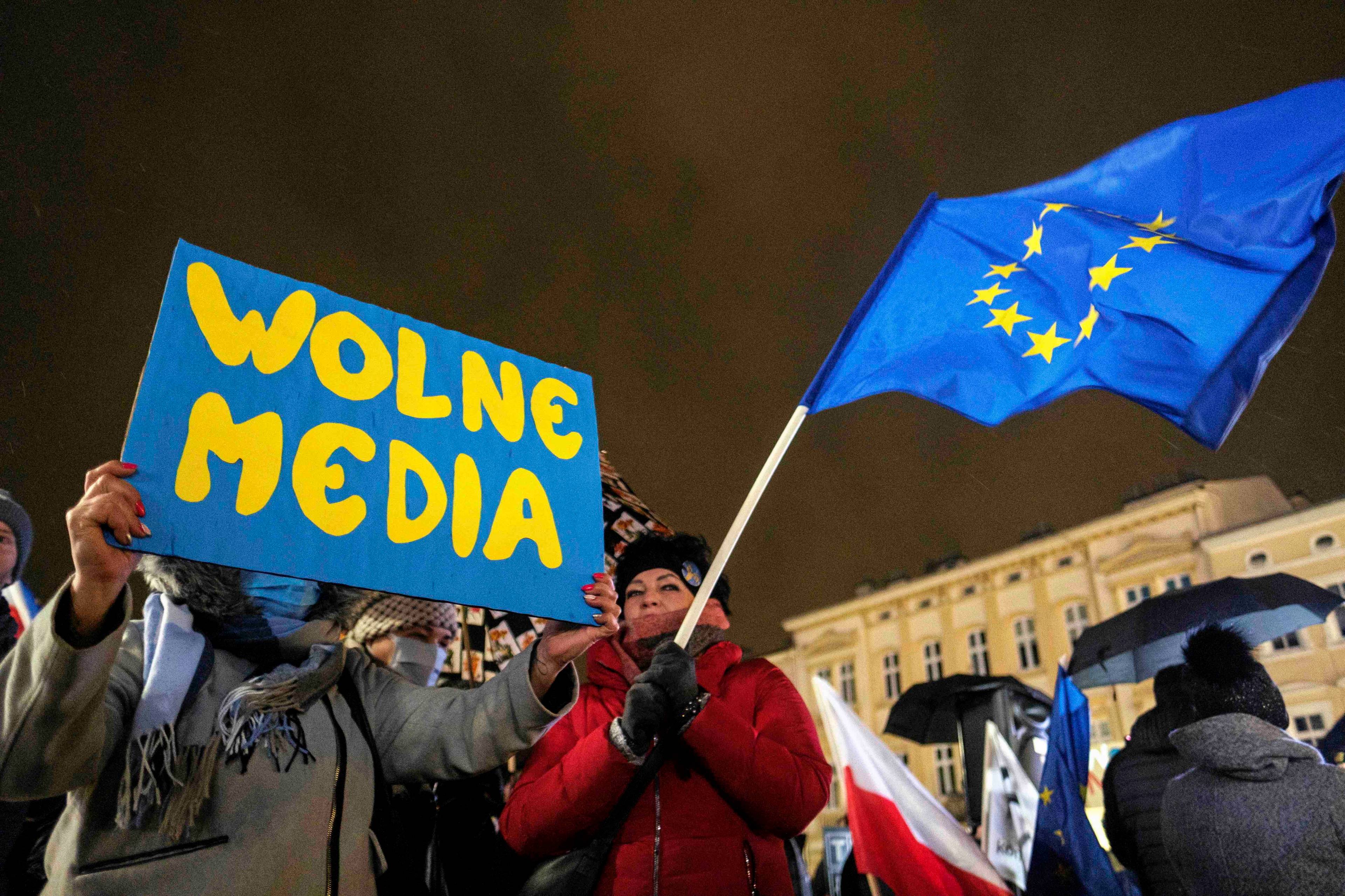 Wieczorna demonstracja, uczestnicy trzymaja plakat z napisem Wolne media oraz flagę Unii Europejskiej