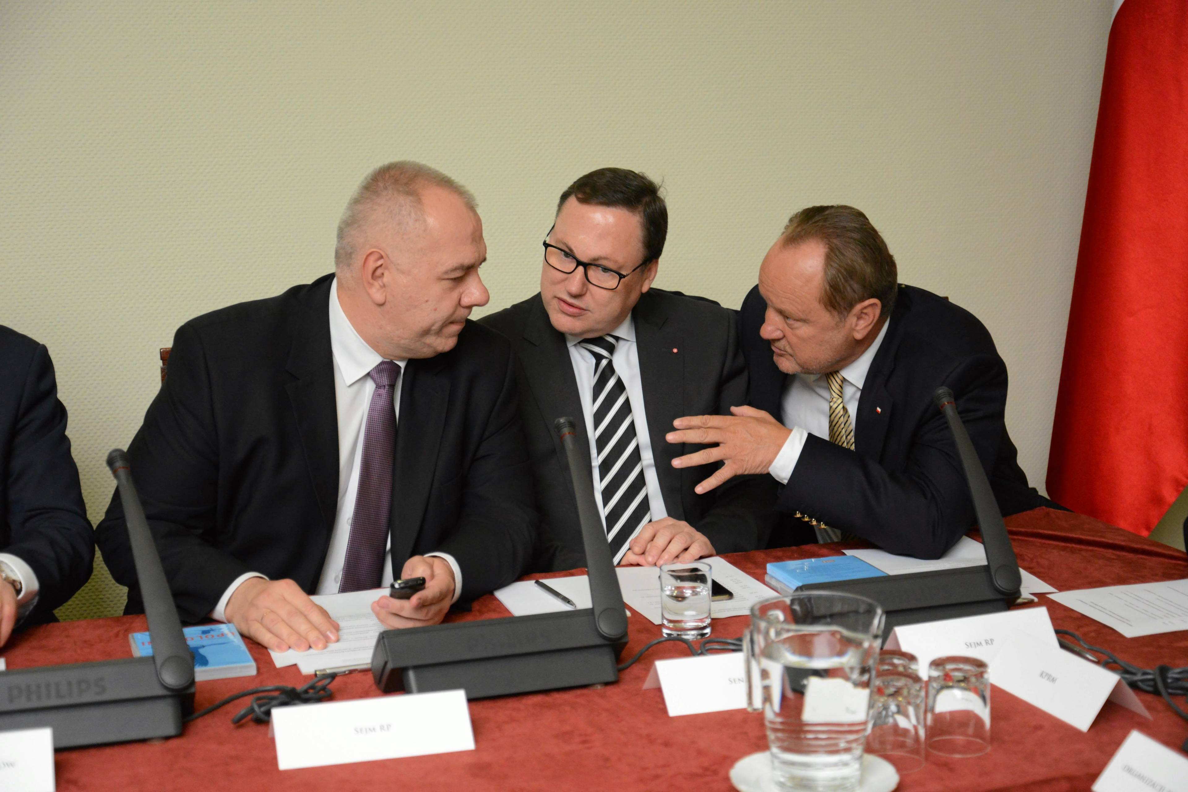 Jacek Sasin, Grzegorz Bierecki i Janusz Szewczak rozmawiają przy stole.