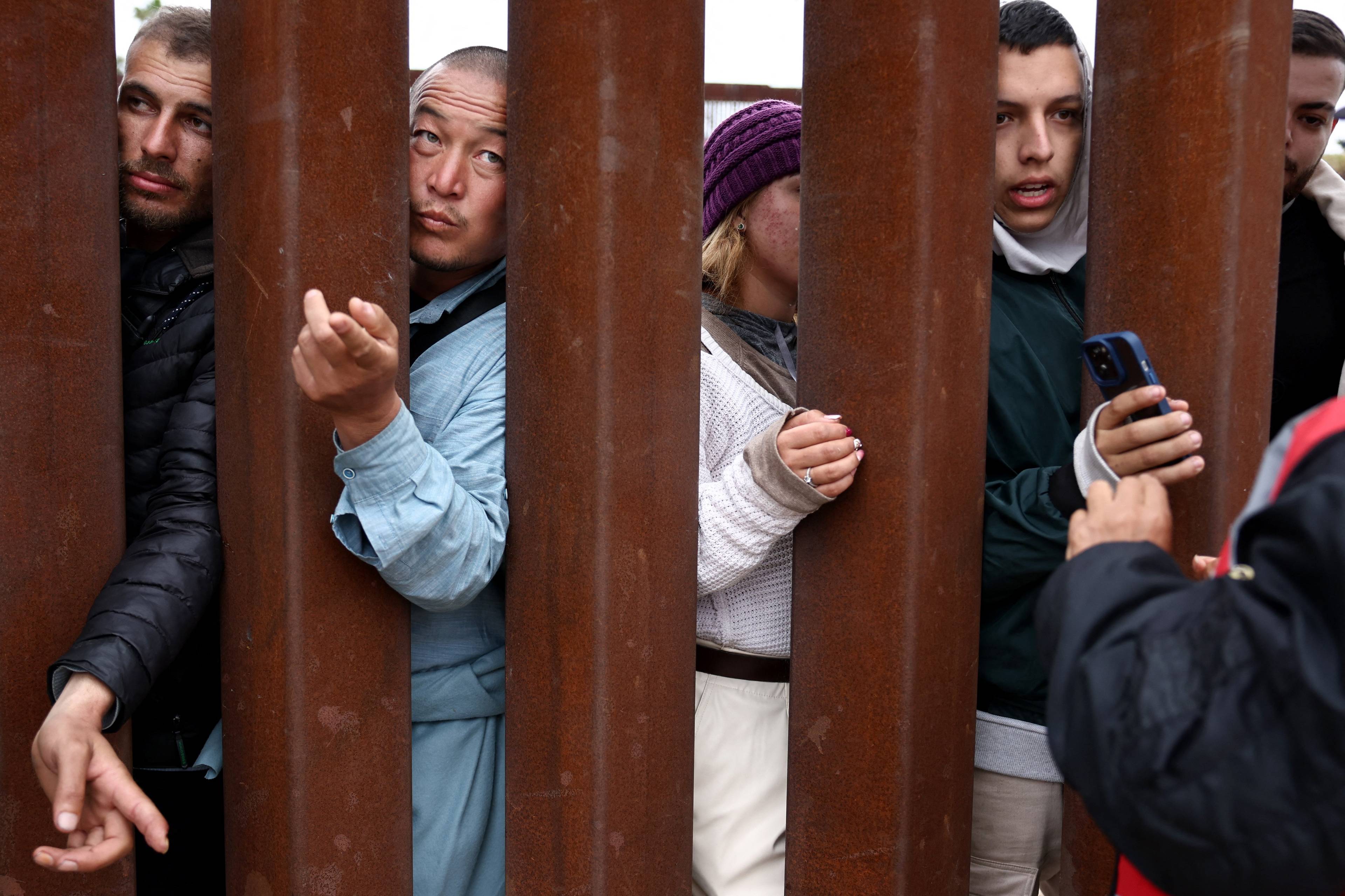 Kobiety i mężczyźni wyciągają ręce przez stalowe pręty muru na granicy USA z Meksykiem