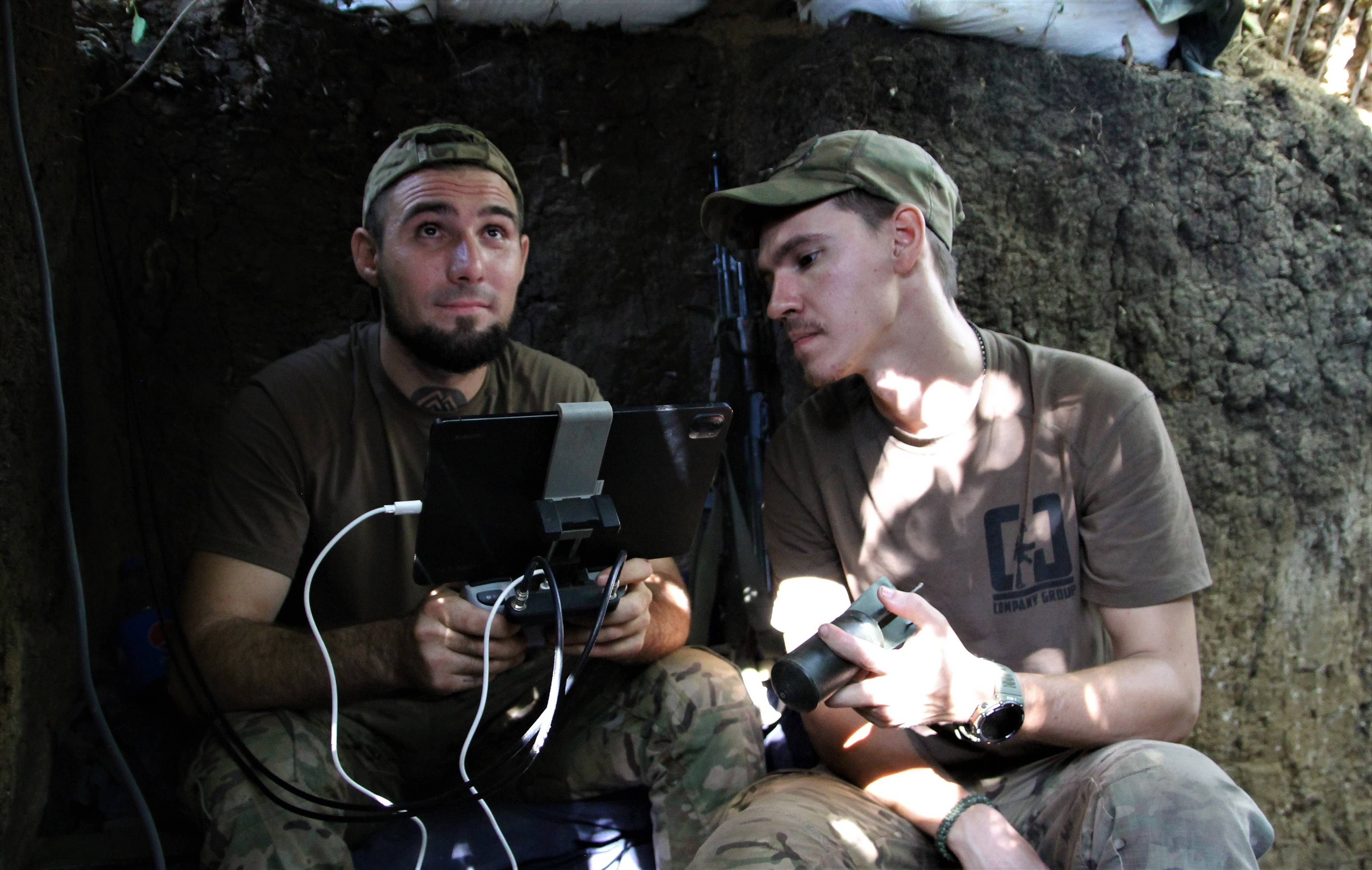 dwaj młodzi żołnierze w letnich mundurach zaglądają do laptopa obsługującego dron