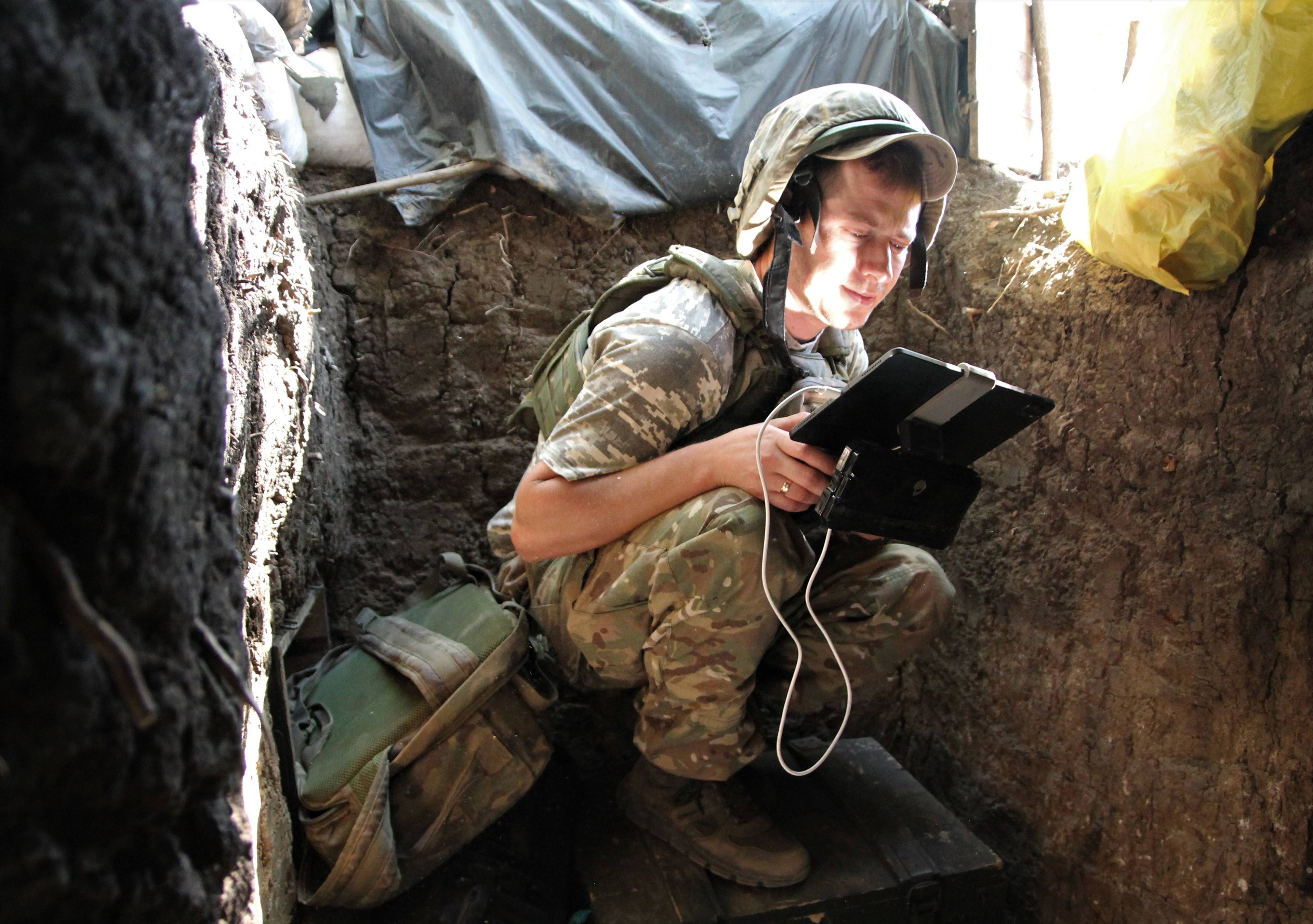 młody żołnierz siedzi w kucki na skrzyni i patrzy w monitor do obsługi drona