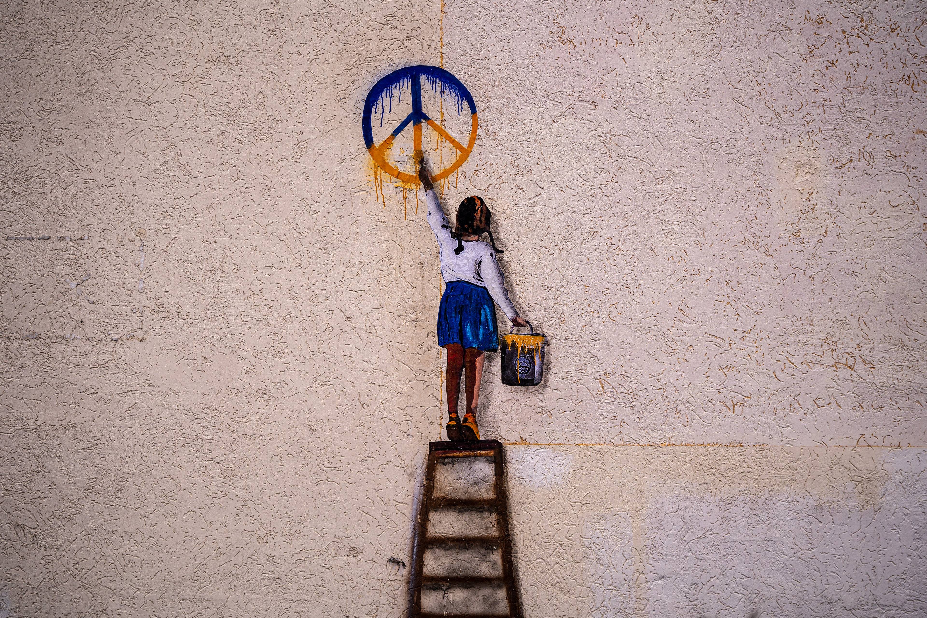 Mural przedstawiający ukraińską dziewczynkę malującą na ścianie pacyfkę, znak pokoju w ukraińskich barwach
