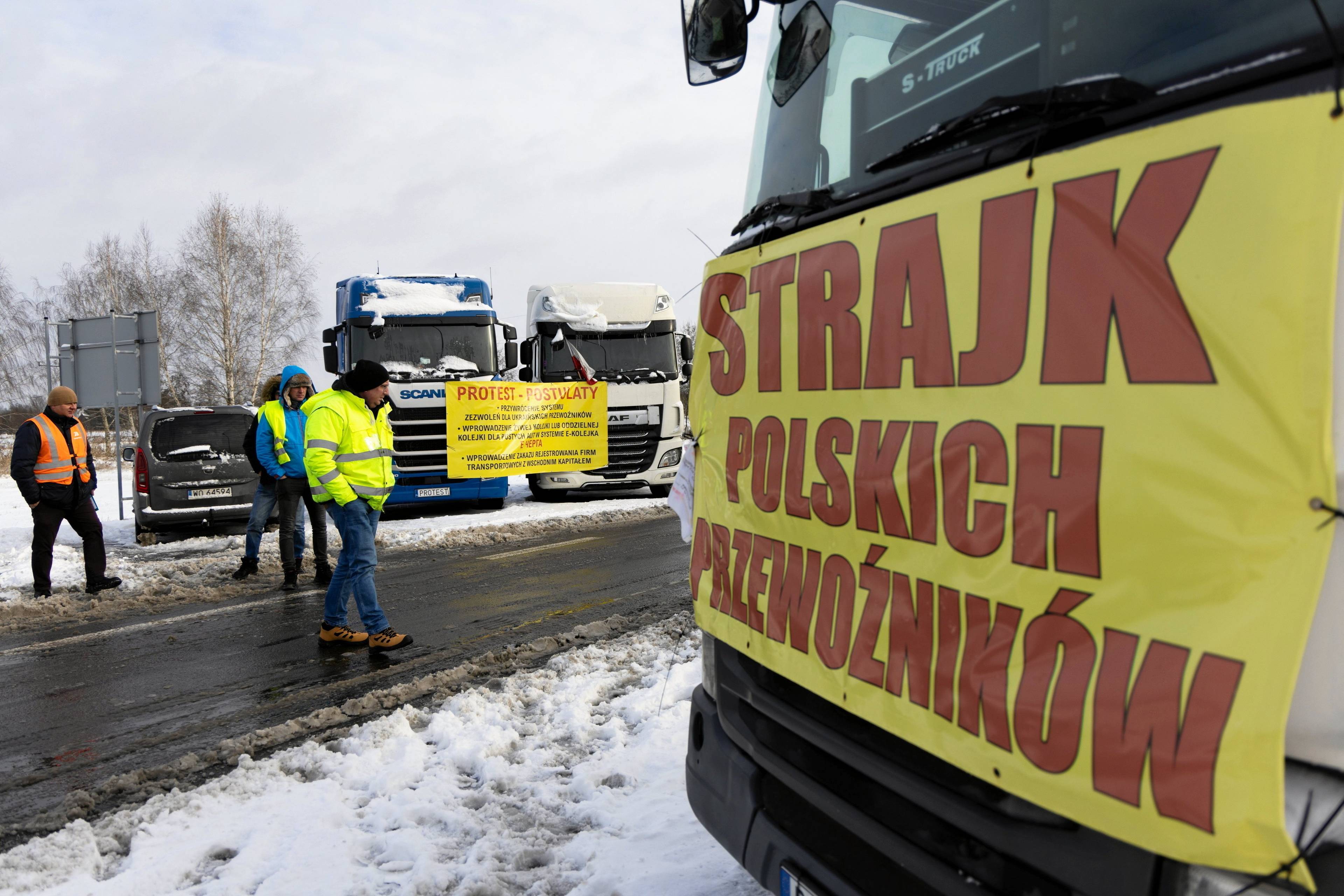 ciężarówka z płachtą z napisem "strajk polskich przewoźników" na masce. w tle inne pojazdy i protestujący w kamizelkach.