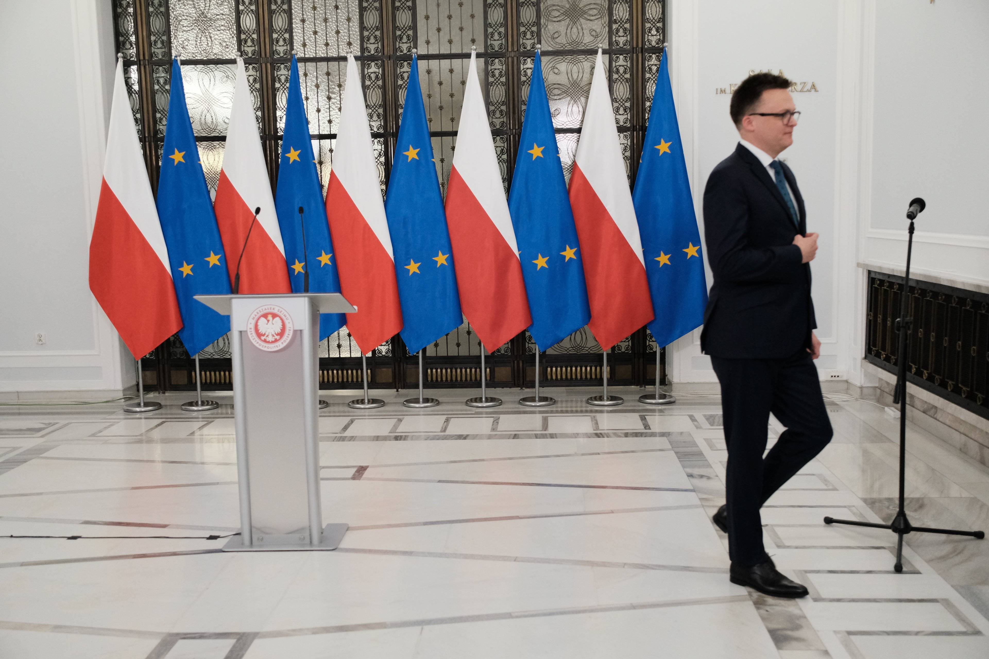 Szymon Hołownia wychodzi z sali po zakończeniu pierwszej konferencji prasowej jako marszałek Sejmu, w tle polskie i unijne flagi