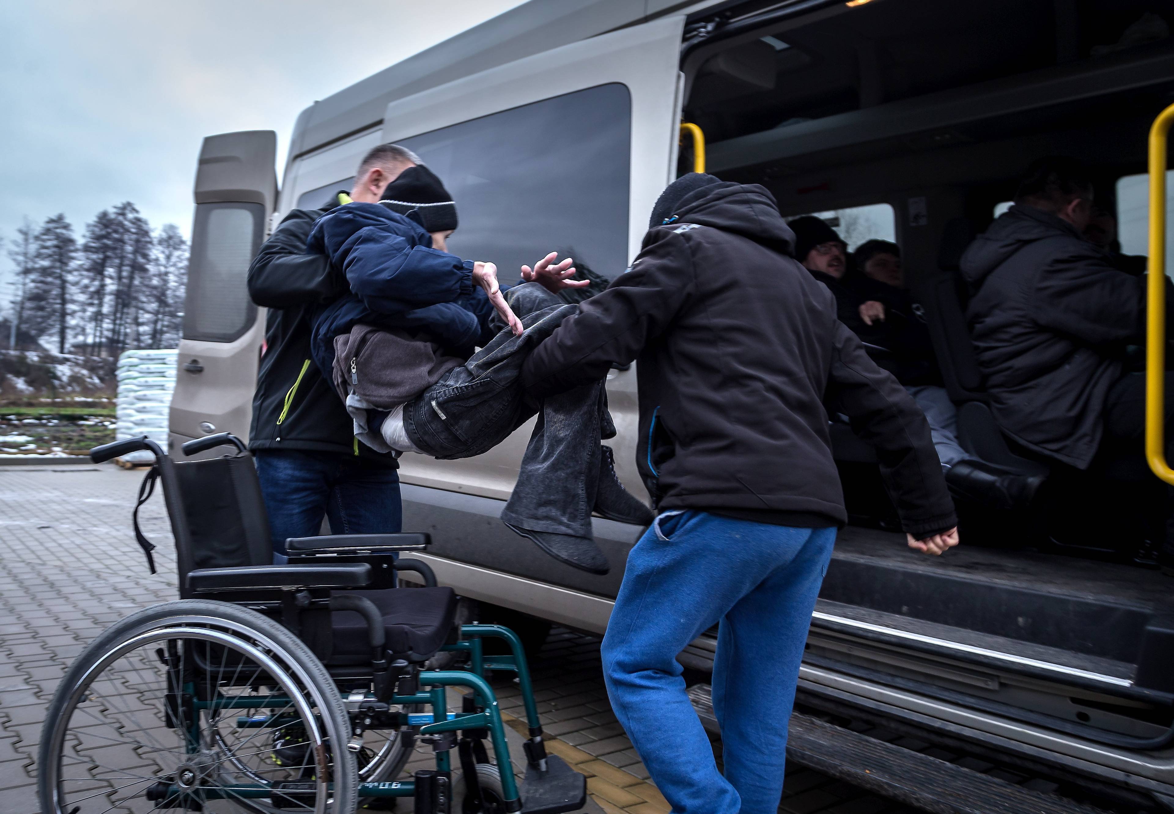 Mężczyzna przenosi chłopca z niepełnosprawnością z wózka do samochodu