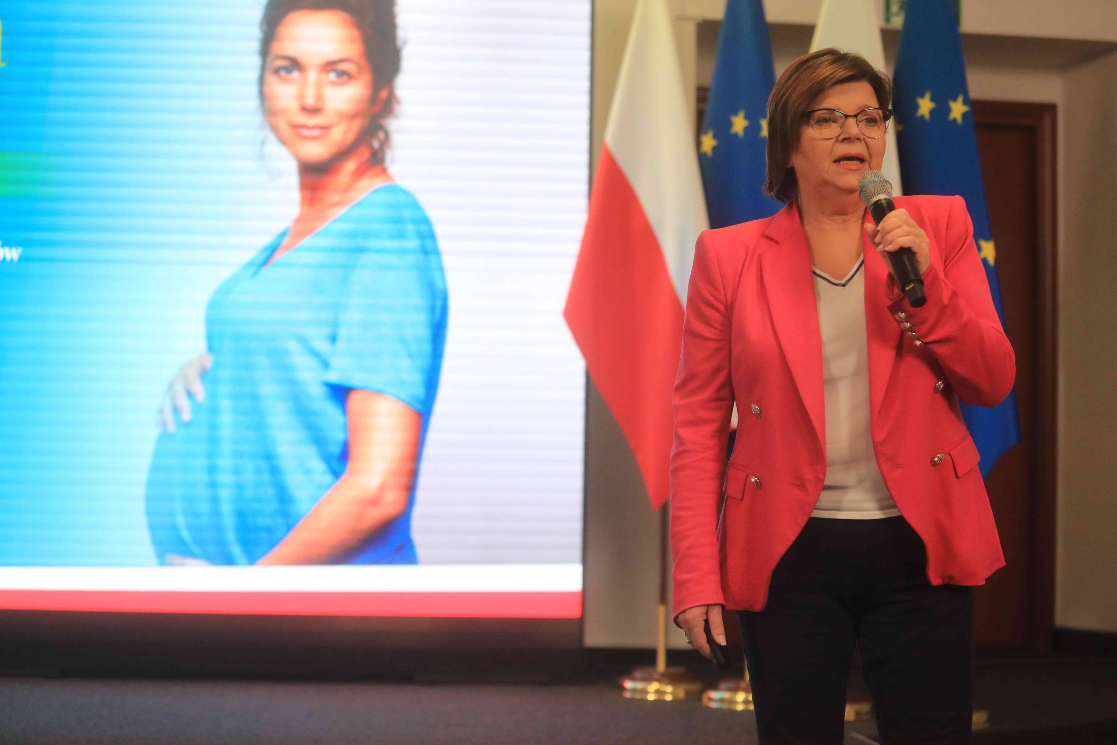 Ministra zdrowia Izabela Leszczyna podczas konferencji prasowej na tle projekcji, przedstawiającej kobietę w ciąży
