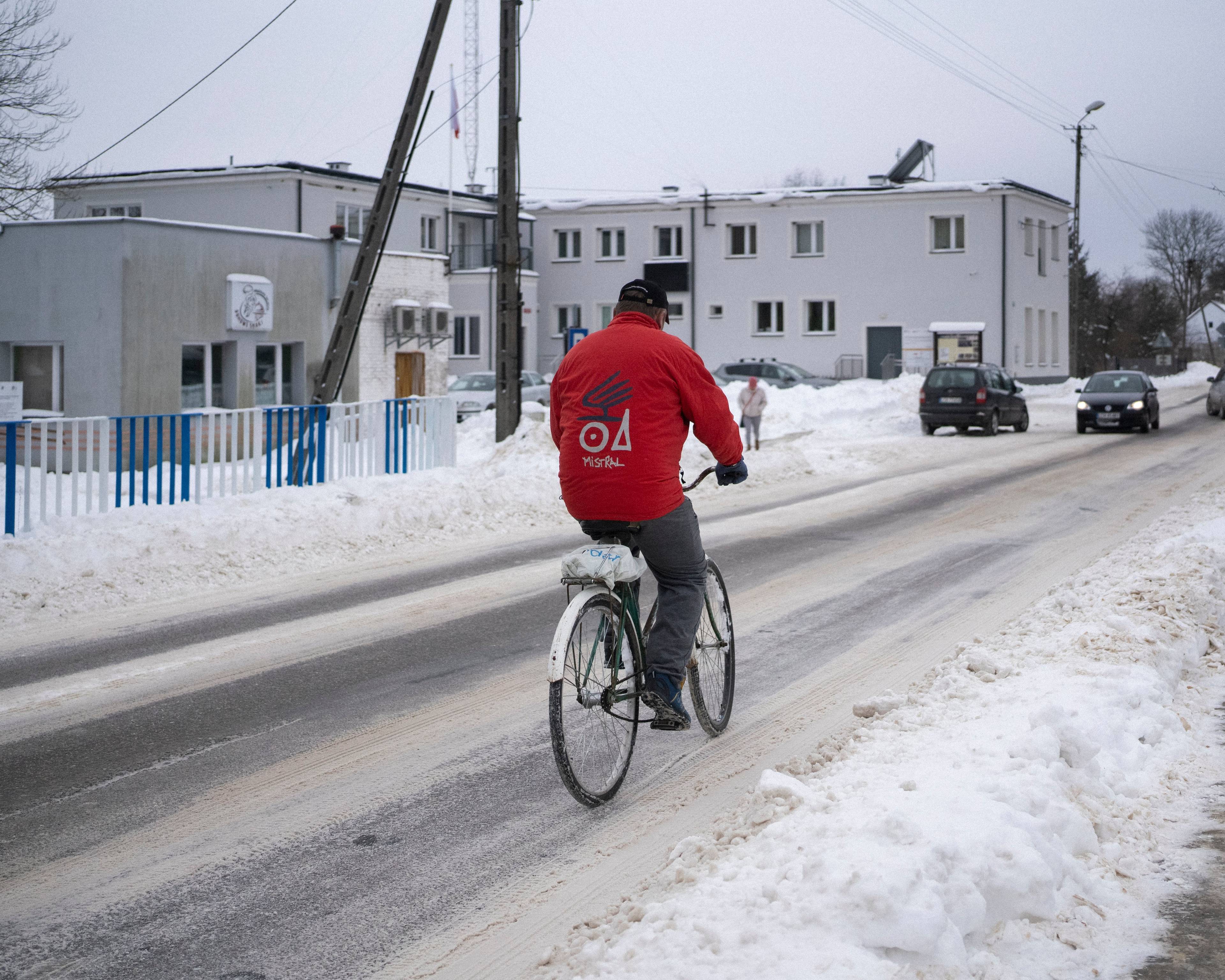 ośnieżona wiejska ulica, na mężczyzna w czerwonej kurtce jedzie na rowerze