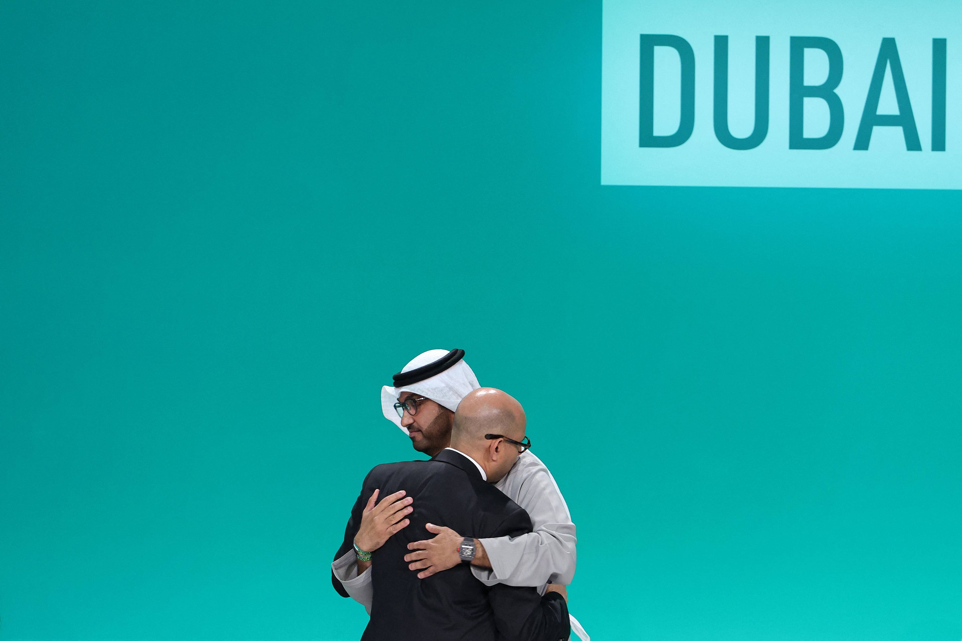 Prezydent COP28 Sultan Ahmed Al-Dżaber i sekretarz wykonawczy Ramowej konwencji Narodów Zjednoczonych w sprawie zmian klimatu (UNFCCC) Simon Stiell obejmują się na scenie podczas sesji plenarnej w trakcie szczytu klimatycznego ONZ w Dubaju. W tle napis Dubai