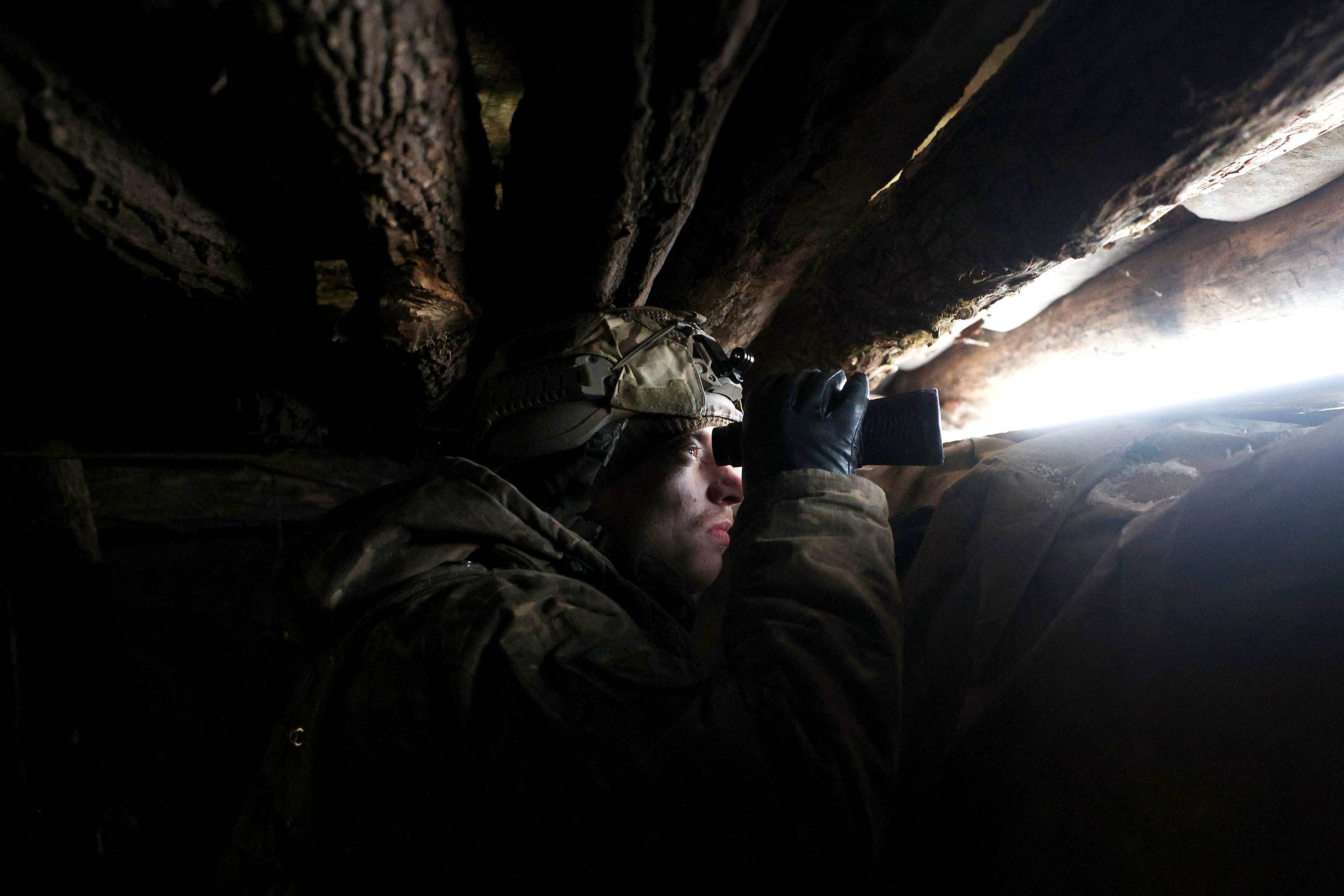 Ukraiński żołnierz patrzy przez lornetkę, zajmując pozycję na linii frontu