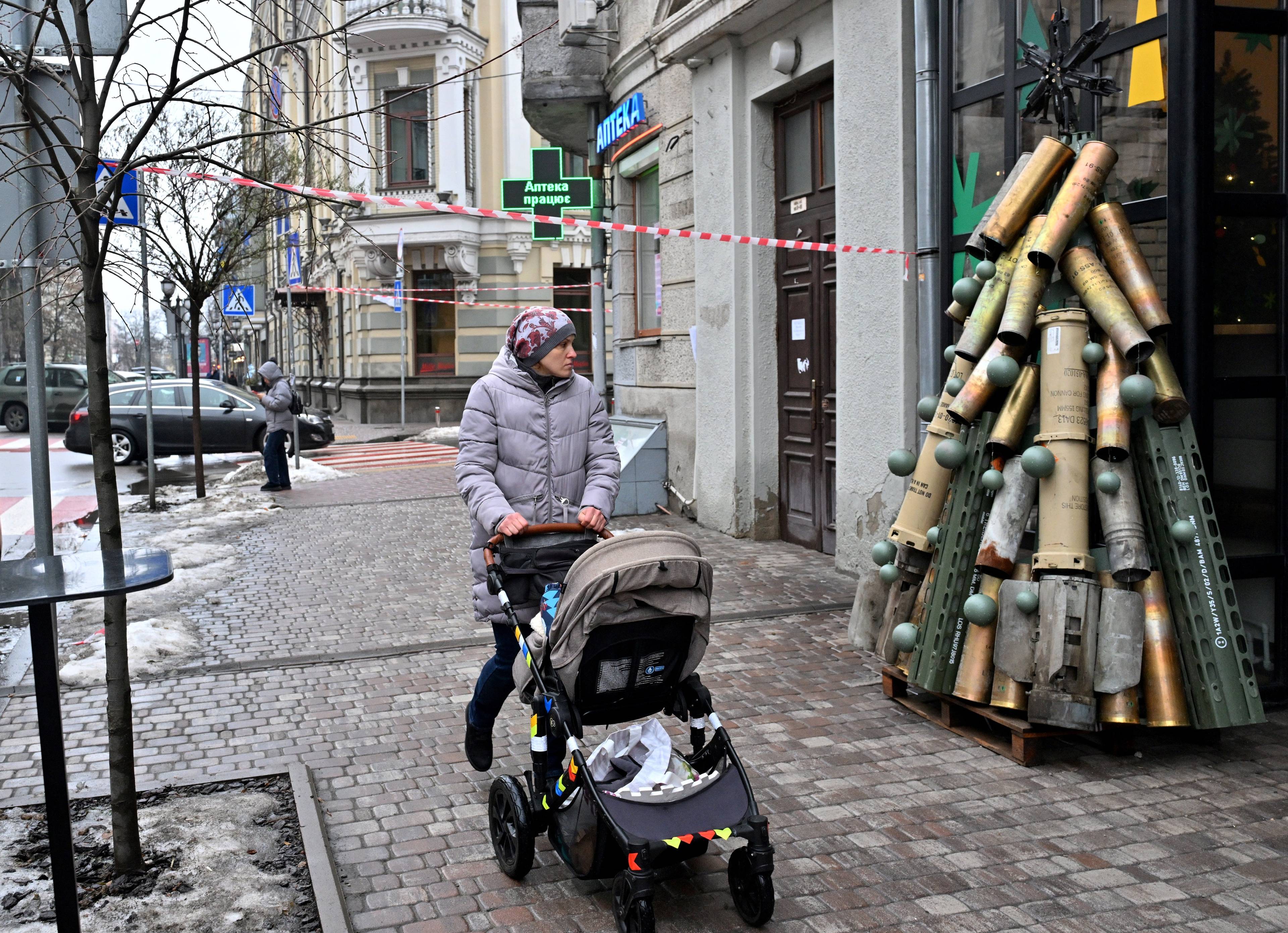 Kobieta z wózkiem dziecięcym przechodzi obok choinki zrobionej z łusek po nabojach.