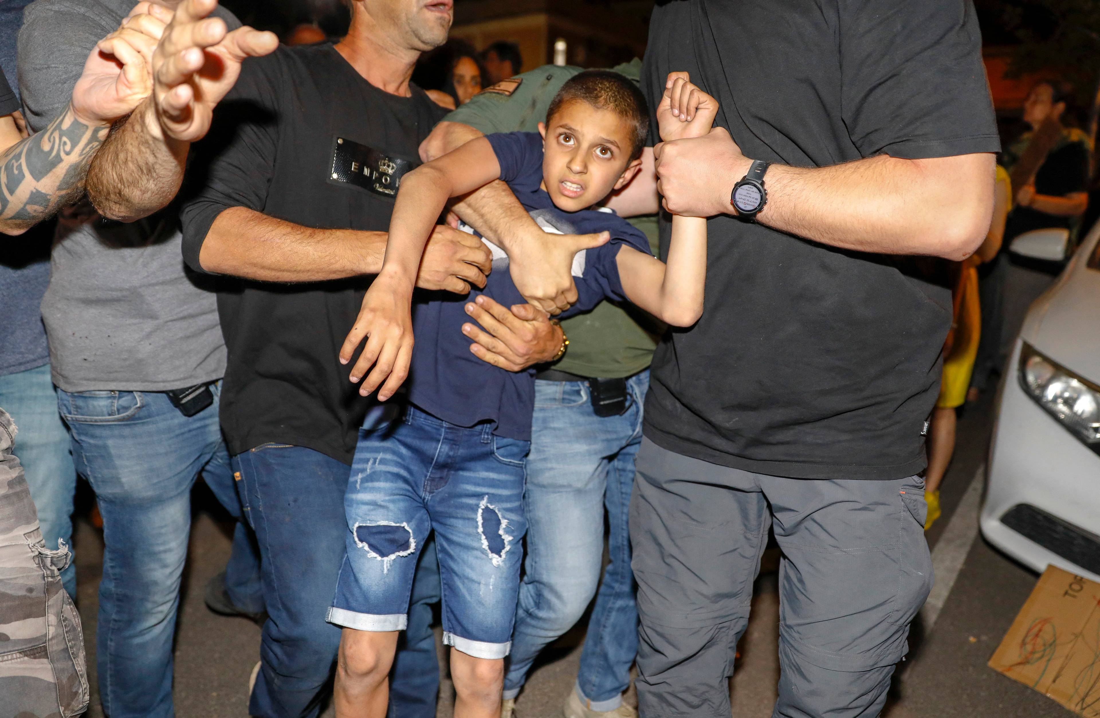 Mężczyźni w dżinsach i tiszertach trzymają za ręce 10-latka. Izrael