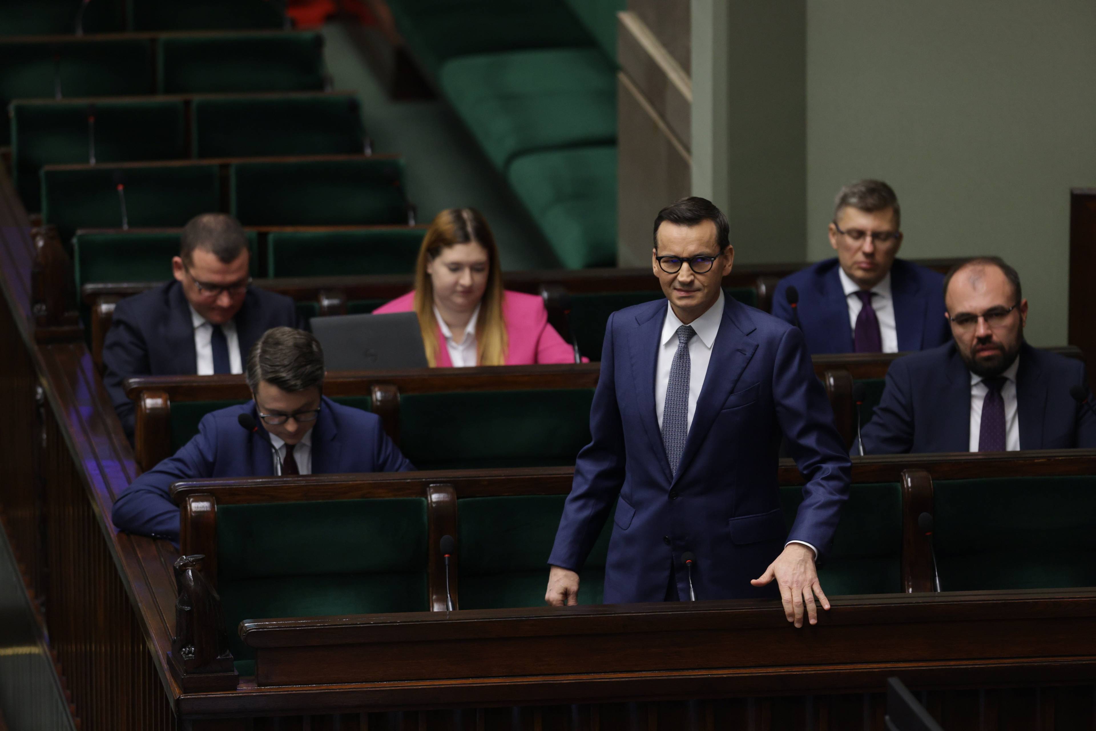 Mateusz Morawiecki stoi w ławach rządowych na sali plenarnej Sejmu. Za nim pozostali członkowie rządu