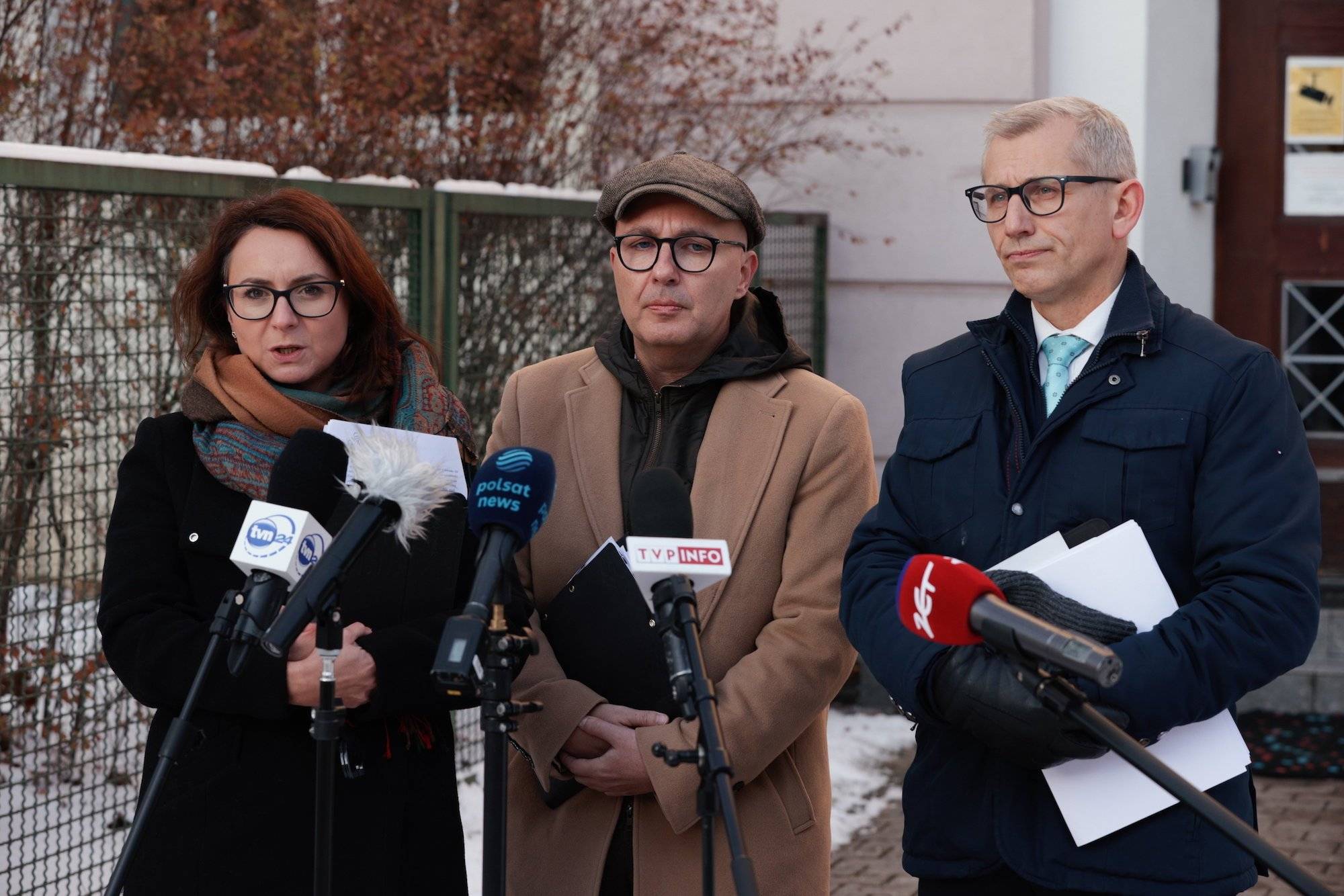 Kamila Gasiuk-Pihowicz, Tomasz Zimoch i Krzysztof Kwiatkowski na konferencji prasowej pod siedzibą KRS. Ubrani w zimowe płaszcze mówią do mikrofonów podstawionych przez media.