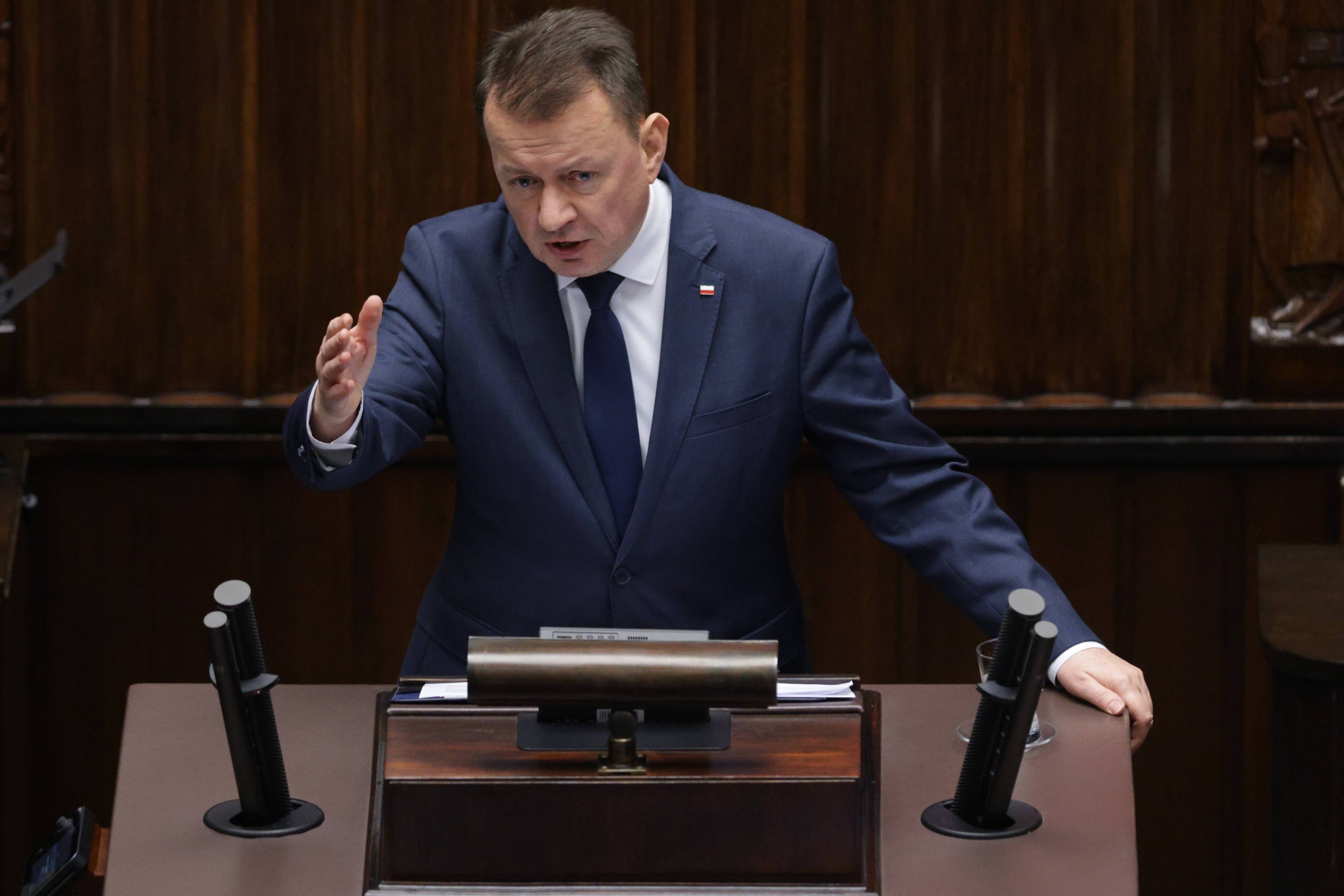 Mariusz Błaszczak z PiS na mównicy sejmowej, wyciąga rękę w stronę słuchających go posłów