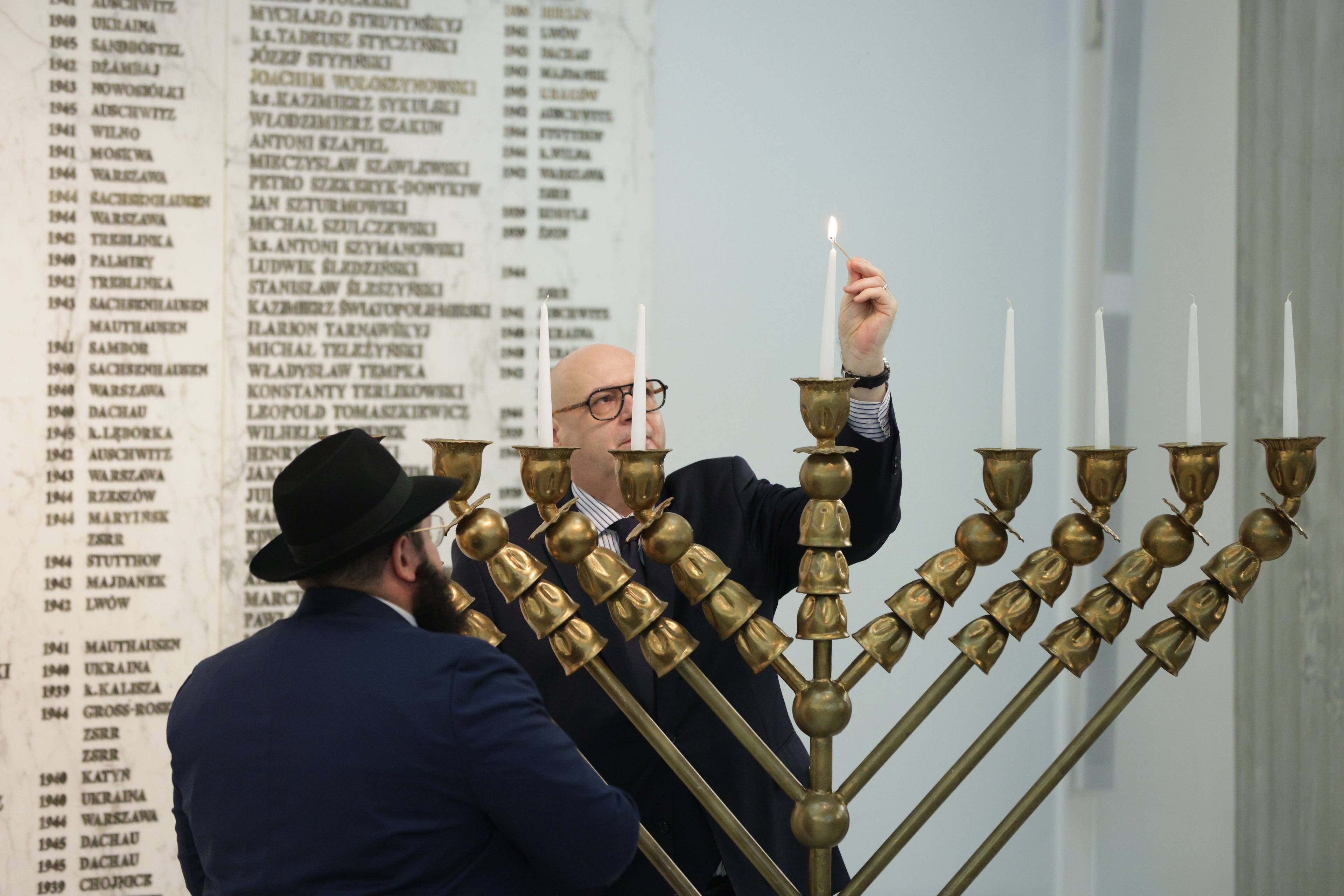 Męzczyzna w garniturze (marszałek Zgorzelski)i mężczyzna w kapeluszu (rabin Szalom Ber Stambler)zapalają świece na siedmioramiennym świeczniku