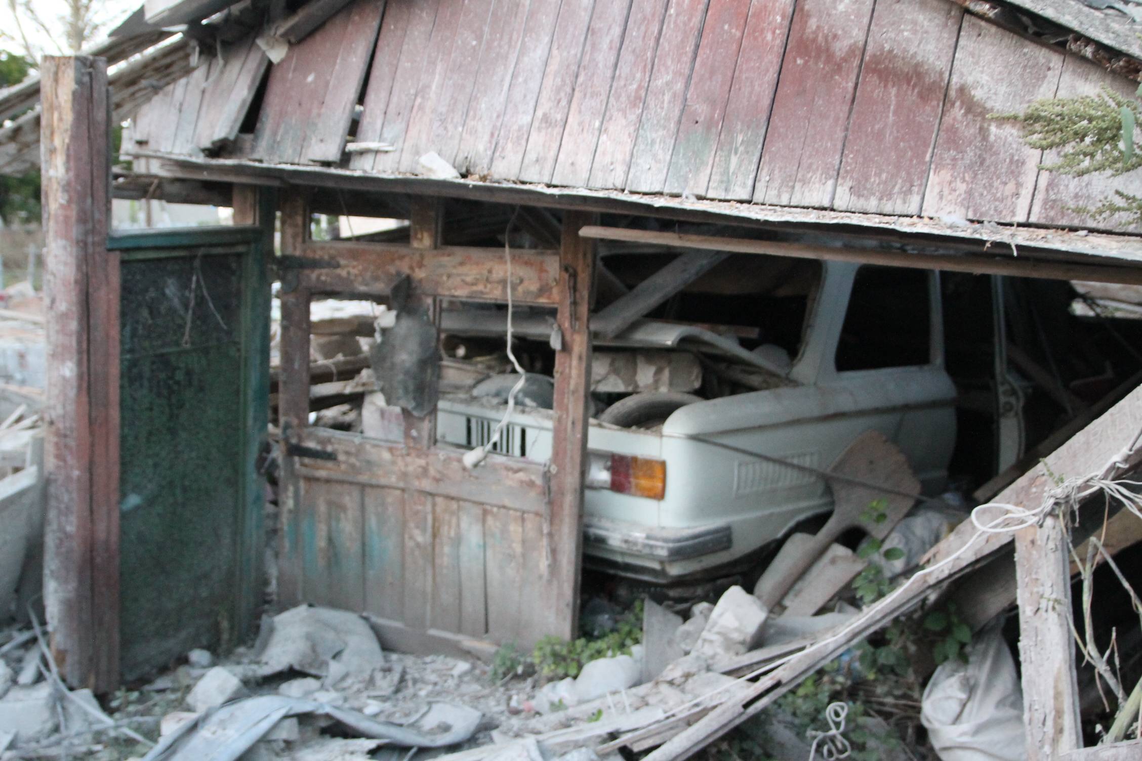 widok zbombardowanej wioski, w zawalonym garażu widać wrak auta