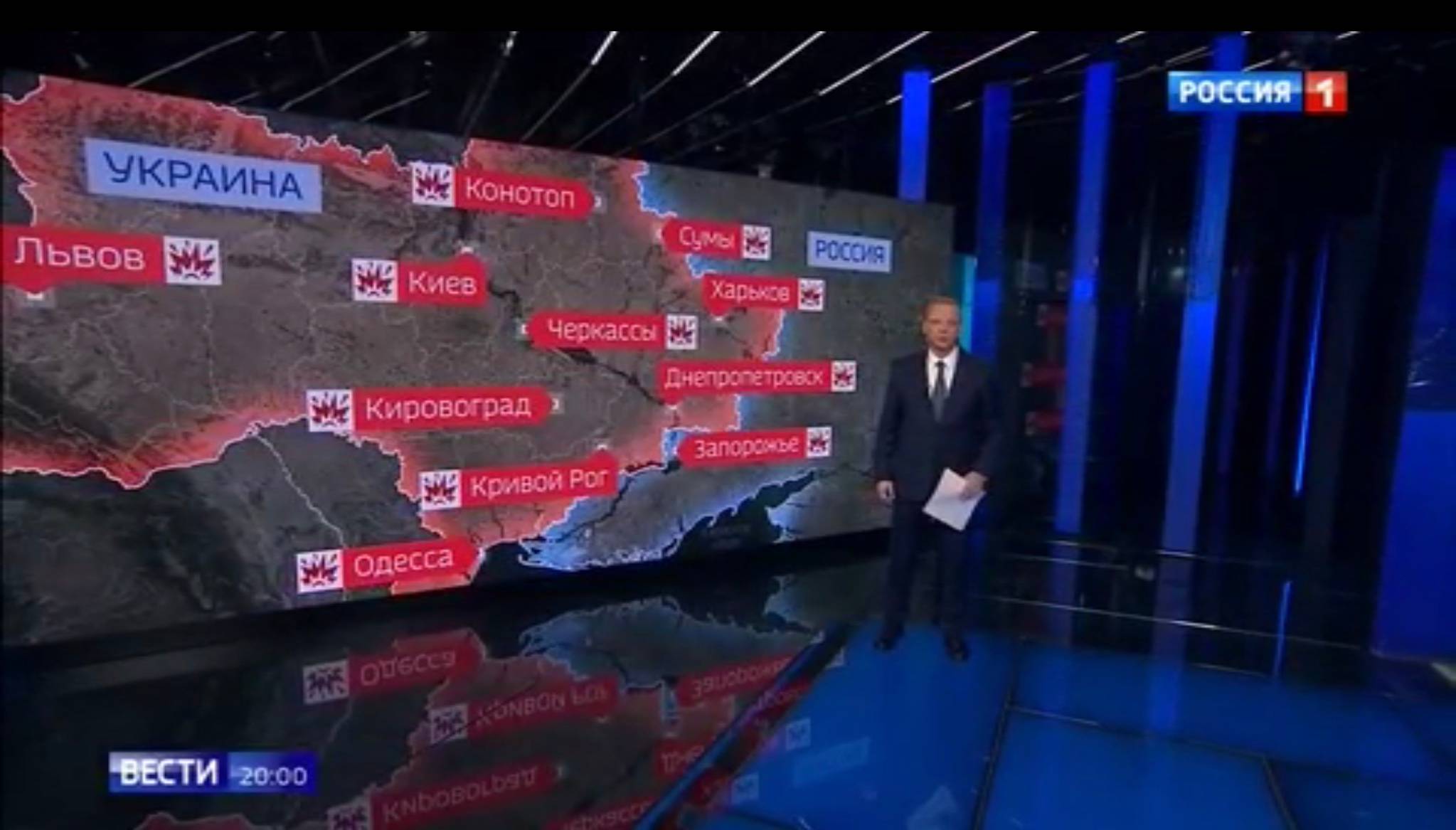 Prezenter w studiu telewizyjnym pokazuje mapę Ukrainy poznaczoną wybuchami
