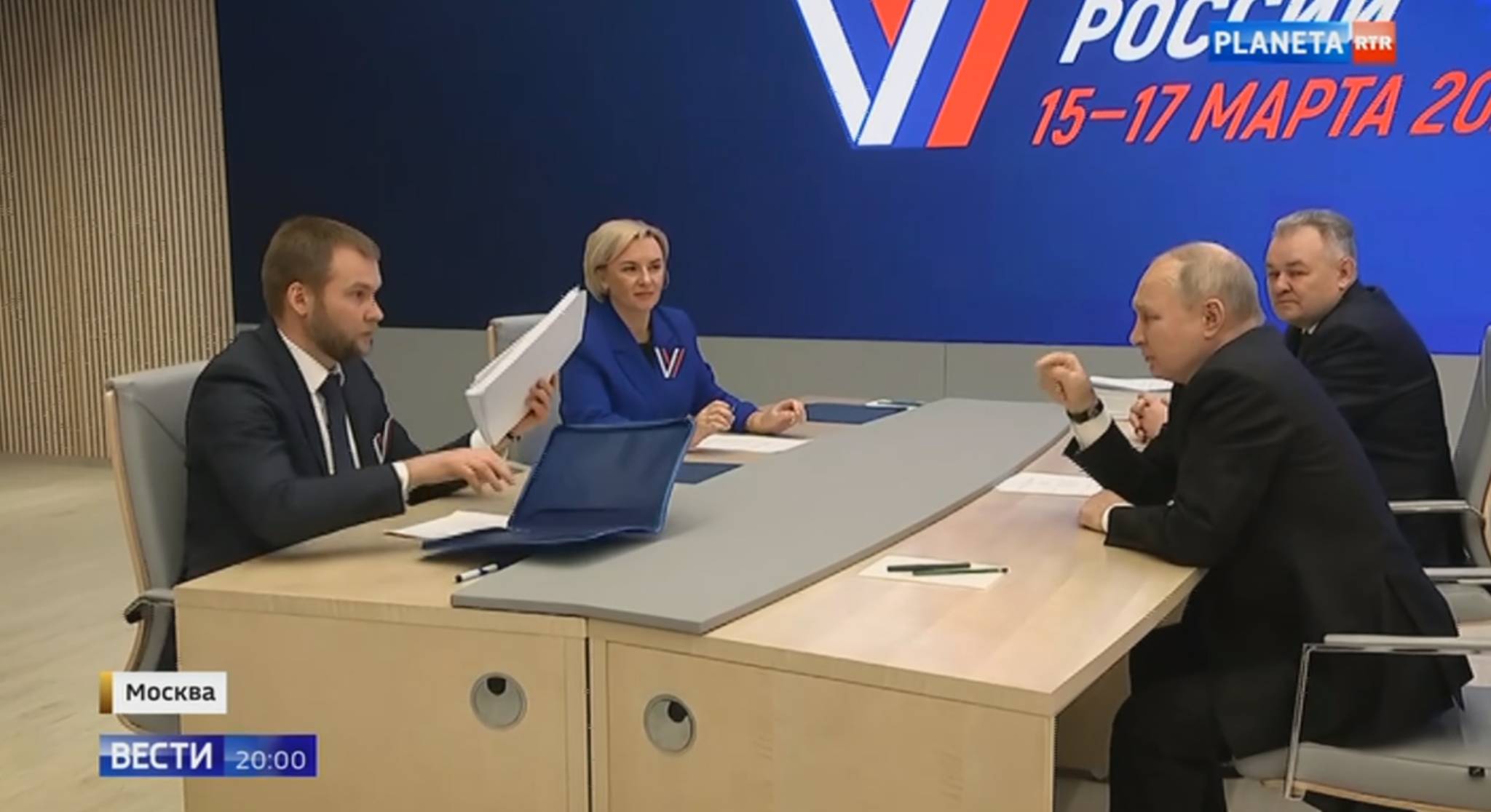 Putin siedzi przy biurku przed dwojgiem urzędników