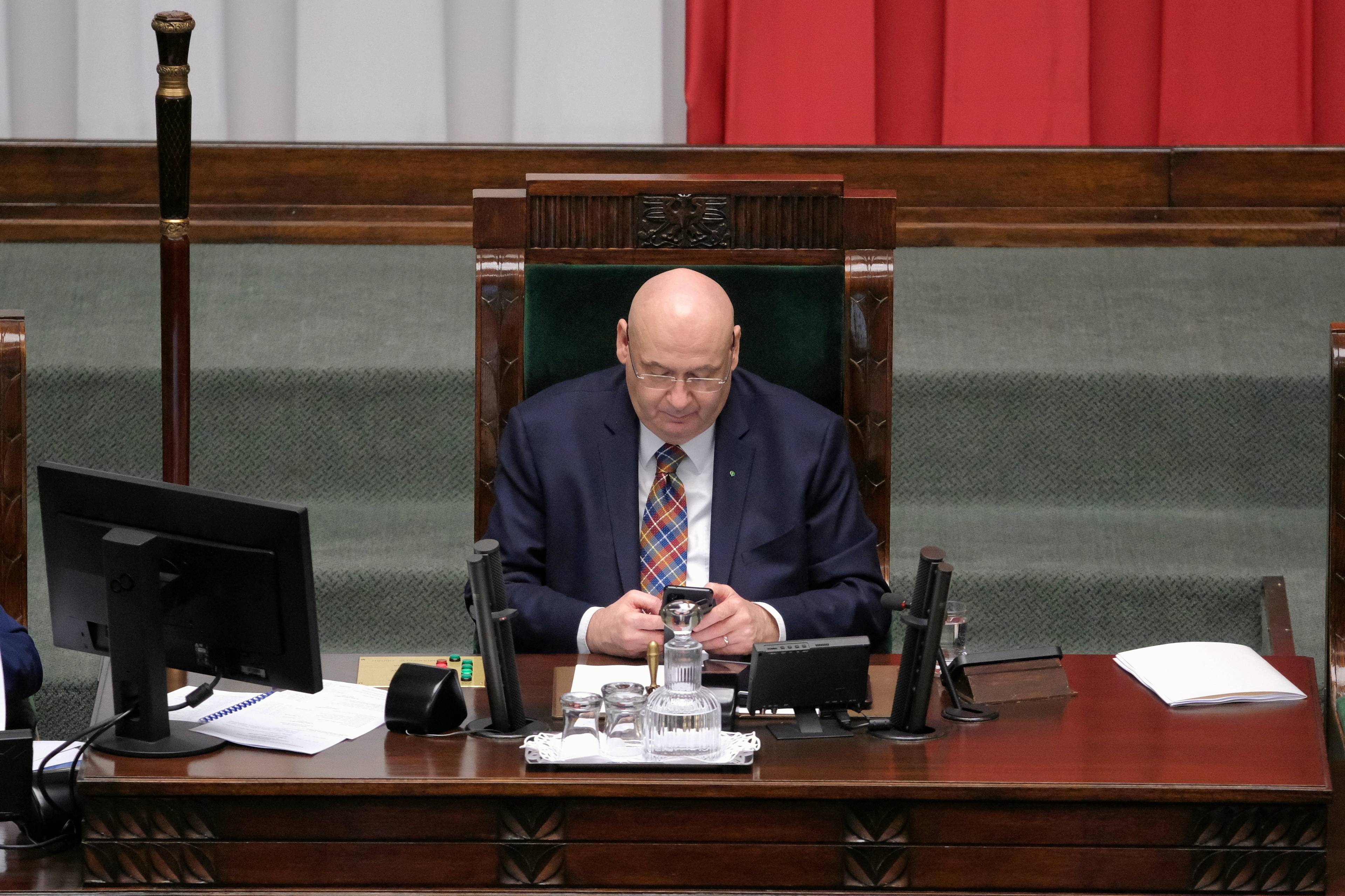 Wicemarszałek Sejmy w fotelu marszałka podczas obrad Sejmu patrzy w swój telefon