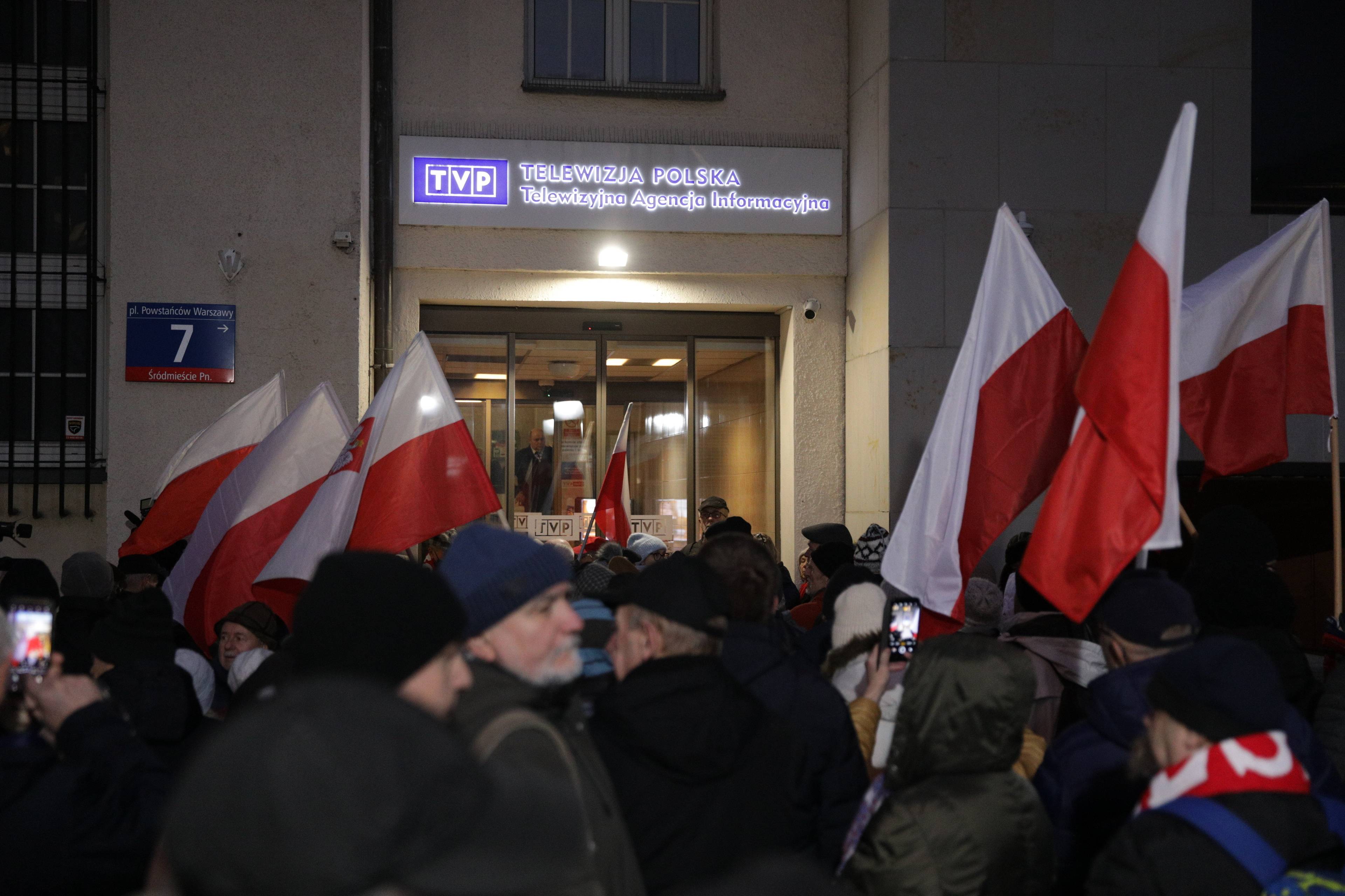Uczestnicy protestu stoją z flagami biało-czerwonymi pod siedzibą TVP Telewizyjnej Agencji Informacyjnej w Warszawie