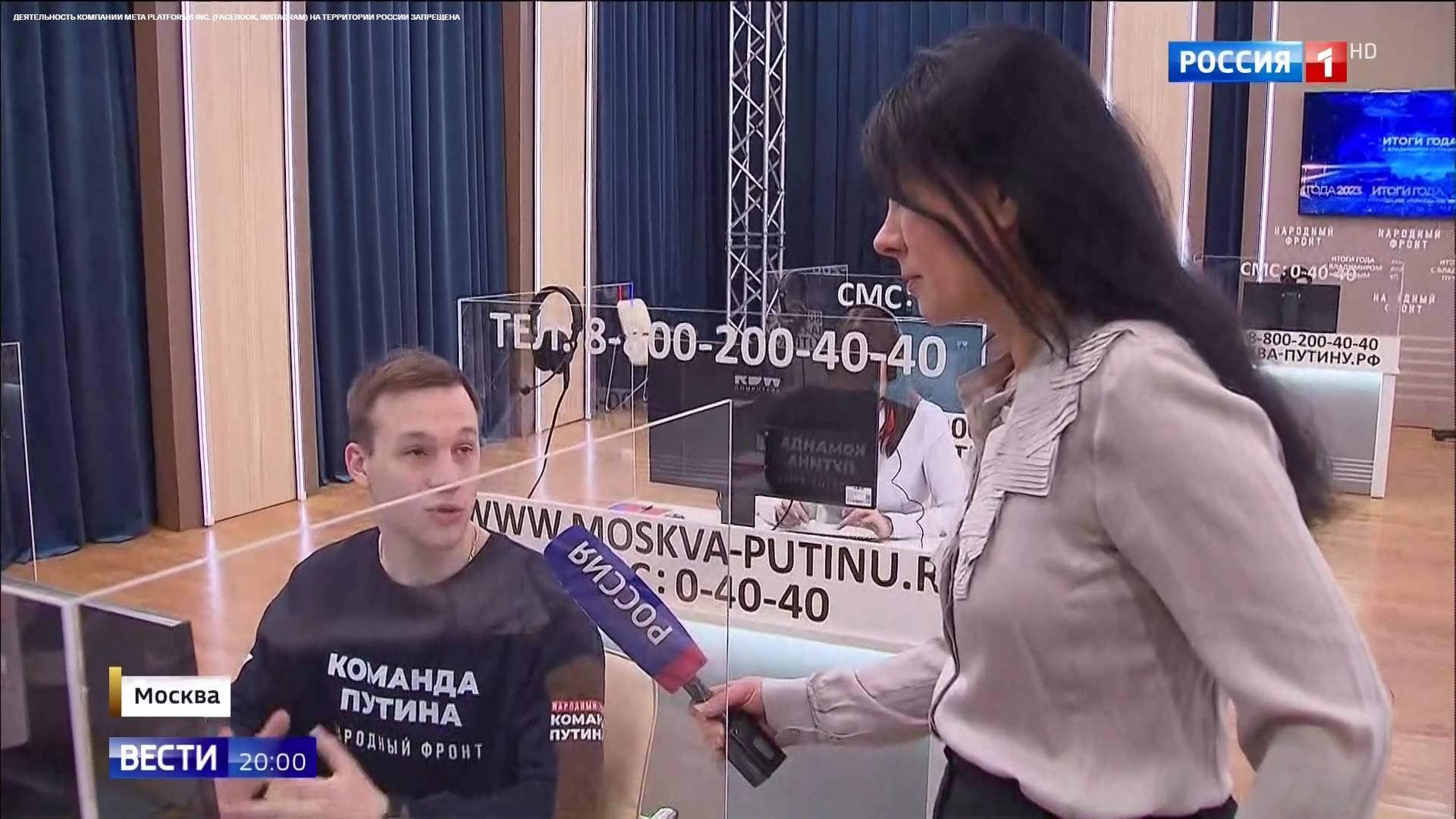 Kobieta z mikrofonem z napisem "Rossija" rozmawia z pracownikiem call center, który na koszulce ma rozysjki napus "Drużyna Putina"