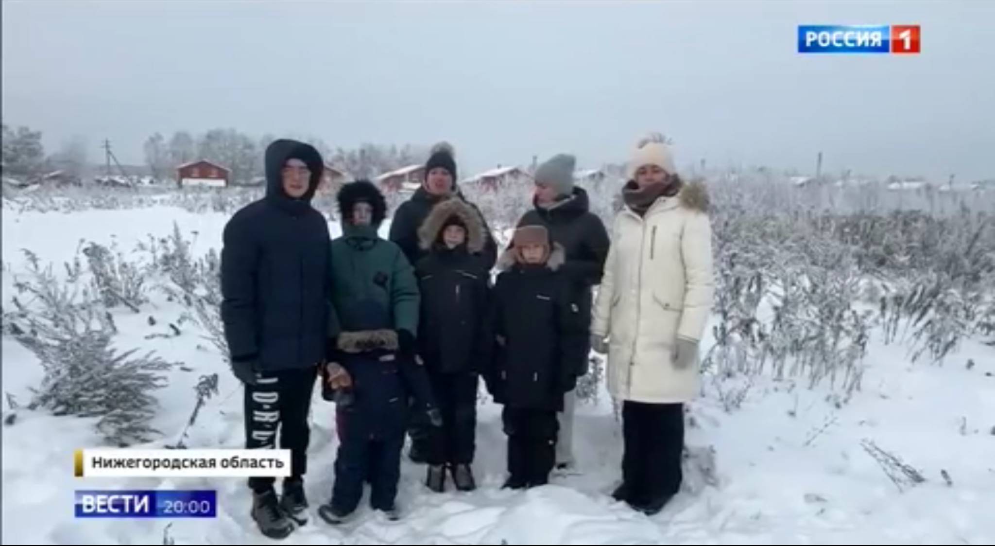 Dzieci i dorośli stoją przed kamerą w zaśnieżonej wiosce