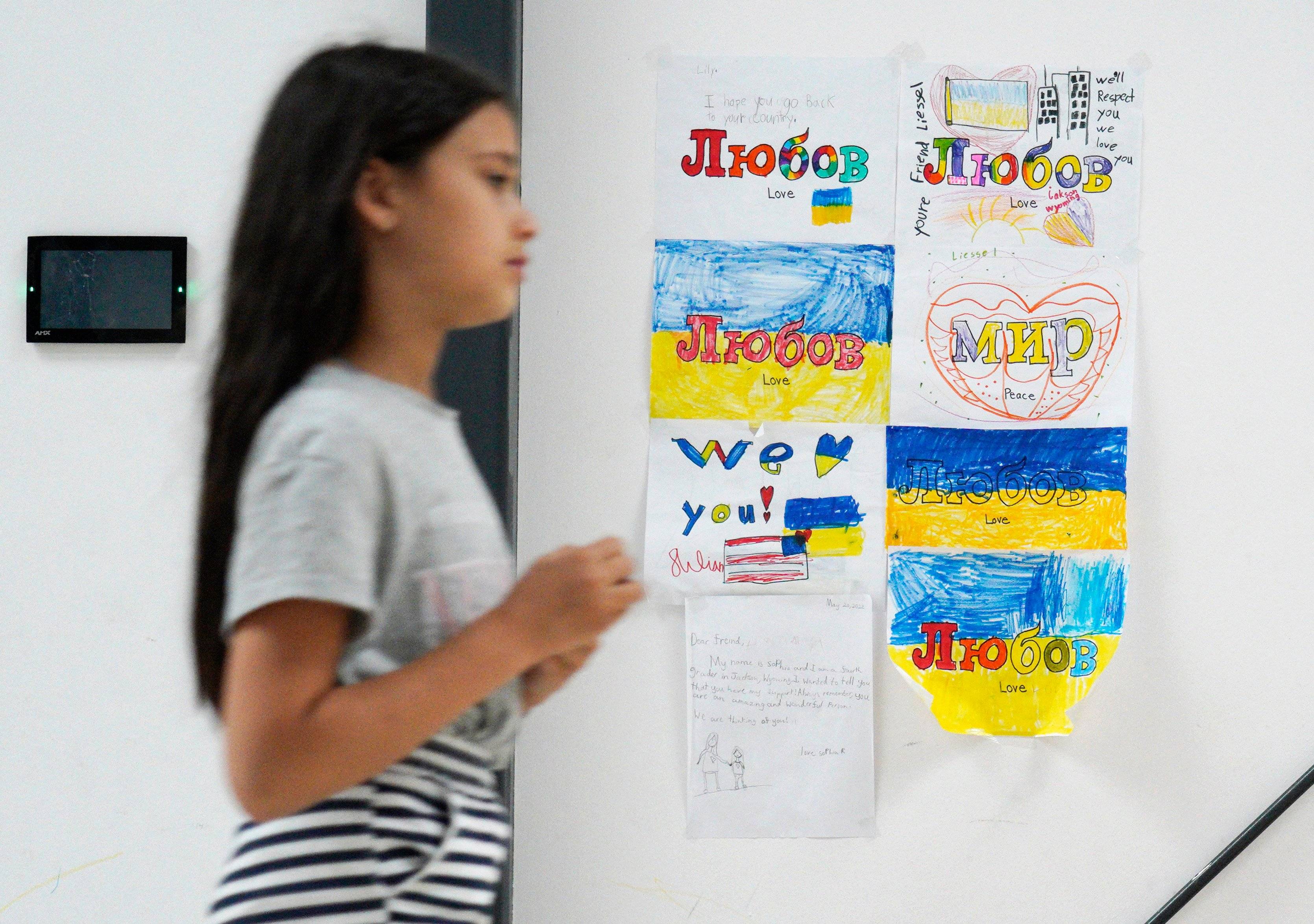 A refugee from Ukraine walks past children drawings reading "love, peace", in the Humanitarian Aid Center set up at the Global Expo exhibition hall in Warsaw on July 15, 2022. The makeshift refugee centre was meant to be a temporary solution but as the war drags on, their lives are still on hold. (Photo by Alik KEPLICZ / AFP) / TO GO WITH AFP STORY BY NELL SAIGNES - TO GO WITH AFP STORY BY NELL SAIGNES