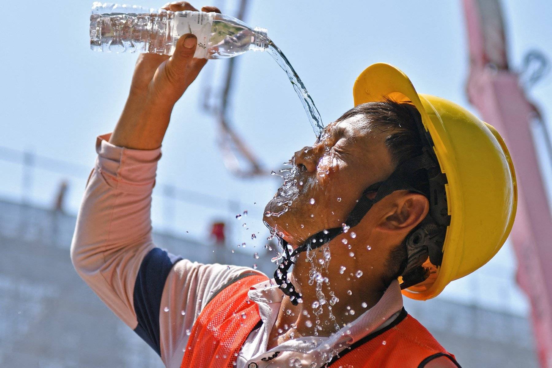 Robotnik budowlany w upale polewa się wodą z butelki. Najcieplejszy rok