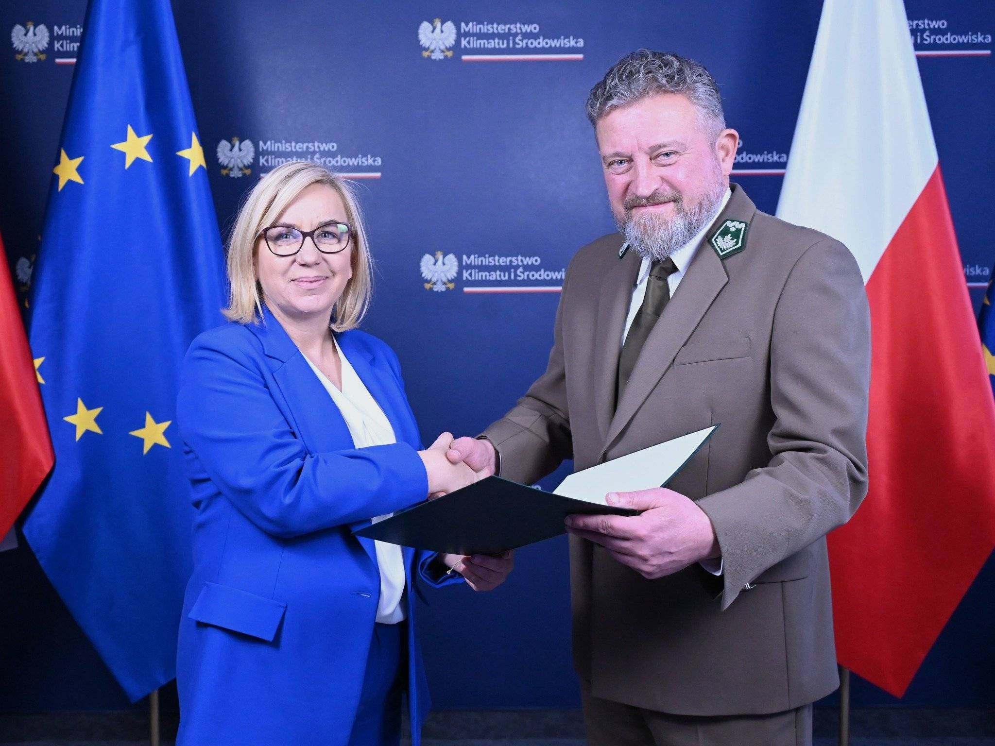 ministra Hennig-Kloska w niebieskim garniturze ściska rękę nowemu dyrektorowi LP Witoldowi Kossowi