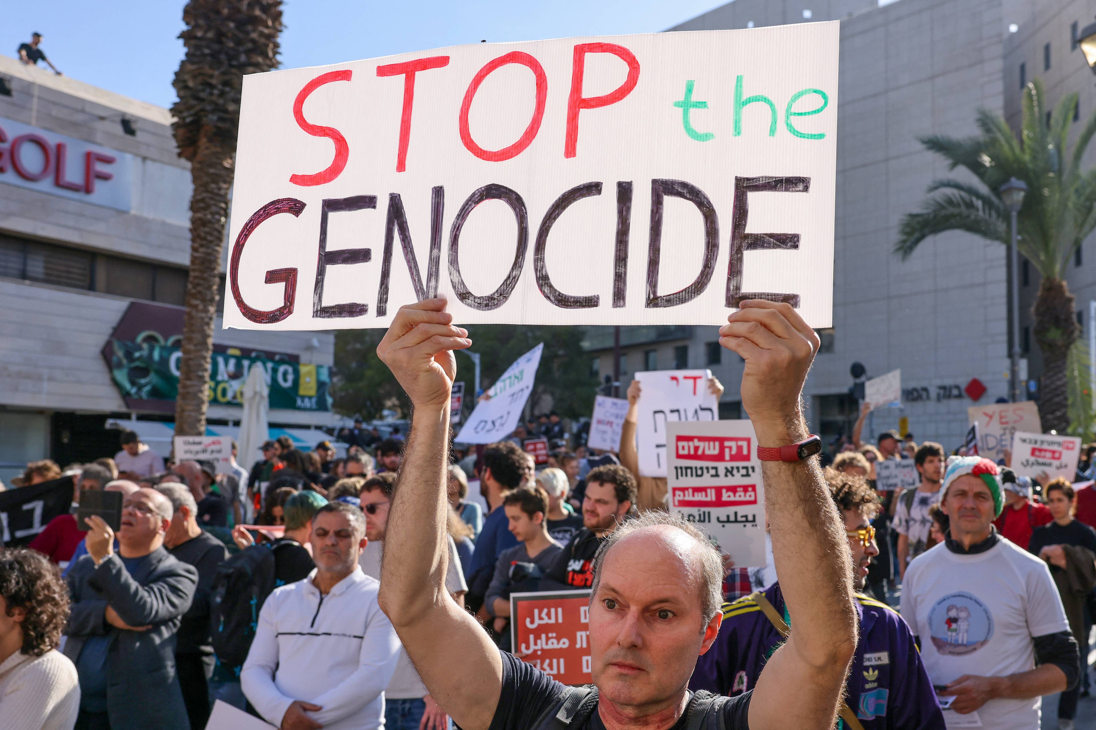 Mężczyzna w tłumie trzymający plakat z napisem STOP GENOCIDE. Miasto Hajfa, Izrael