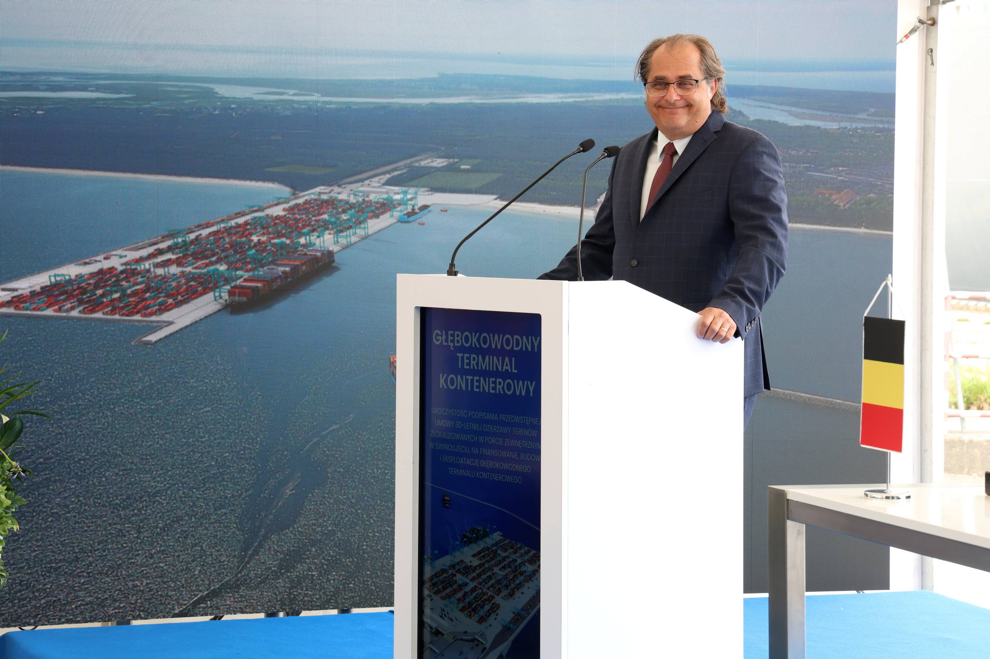 Minister Marek Gróbarczyk stoi przy pulpicie. W tle wizualizacja terminala kontenerowego