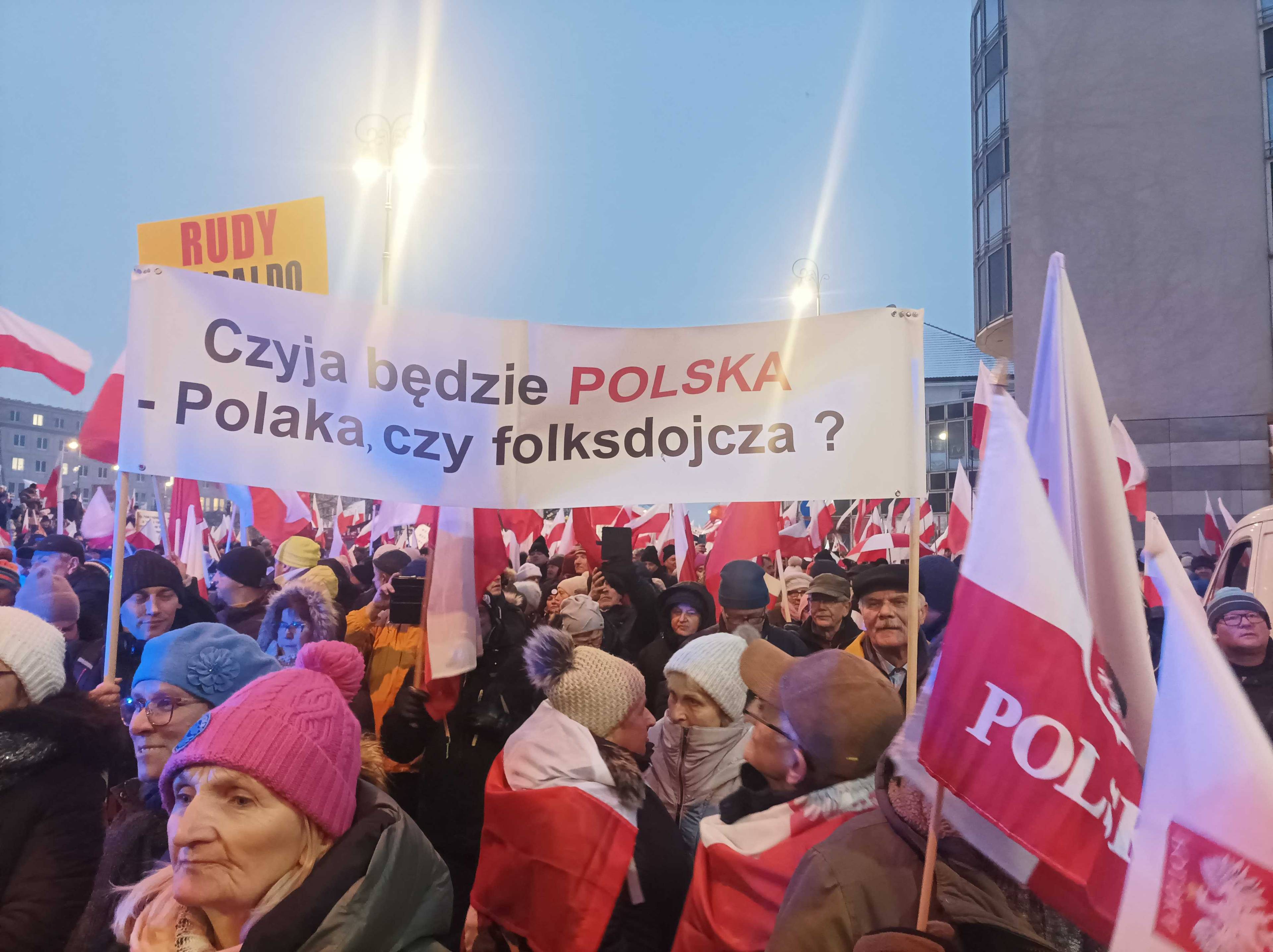grupa ludzi z transparentem i polskimi flagami